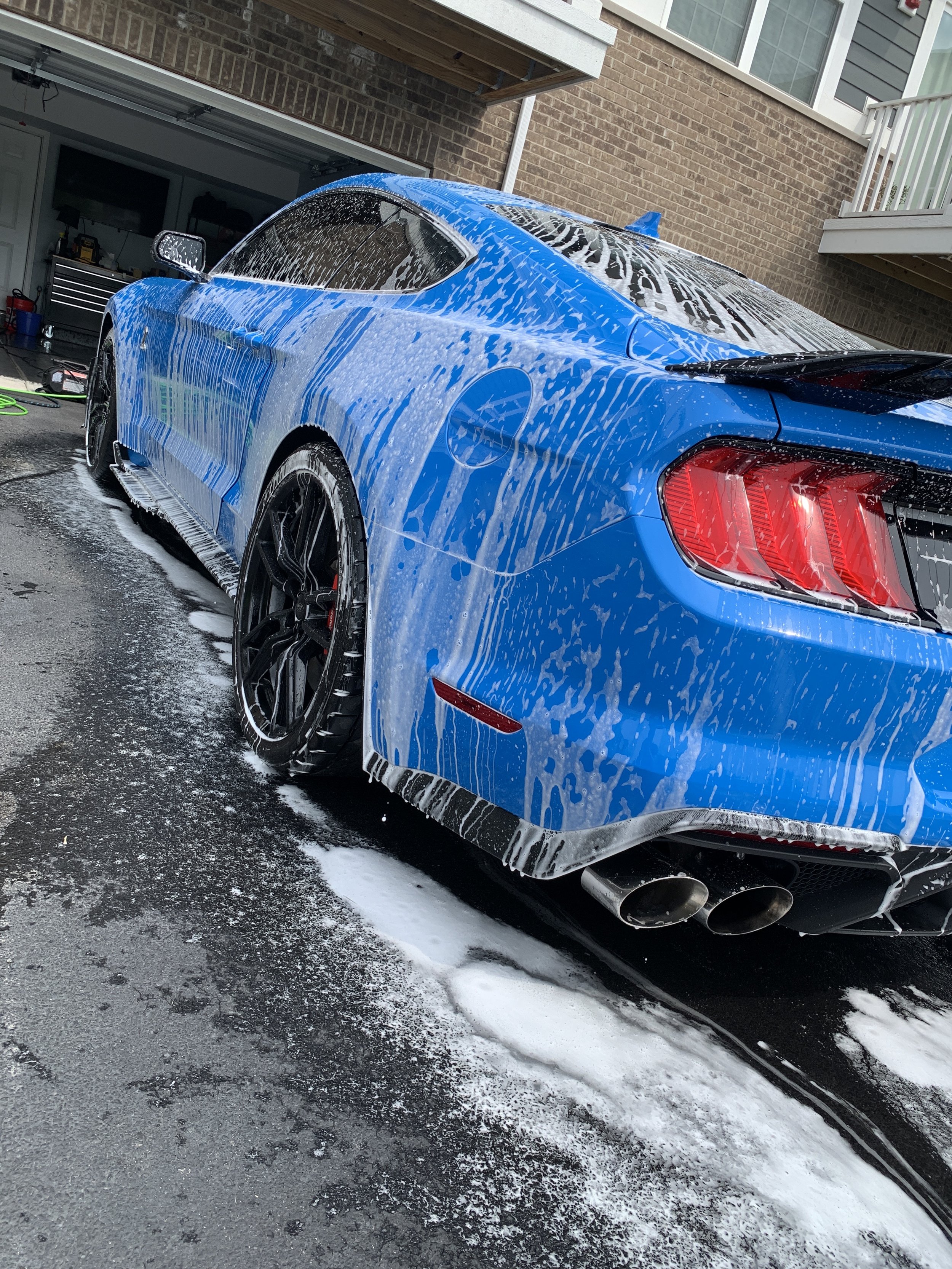 Blue sports car being washed with soap and foam in a driveway.