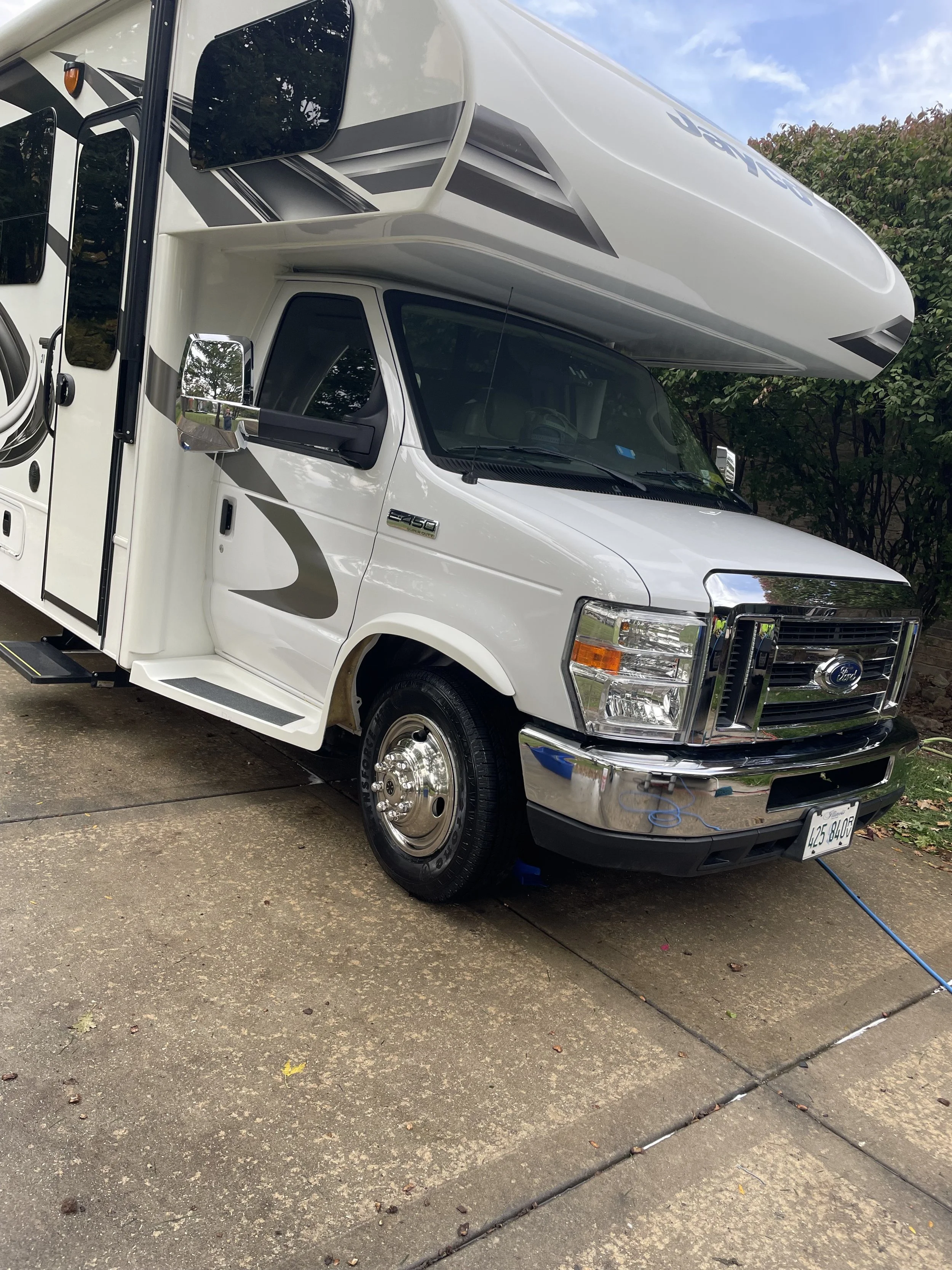 White Ford RV parked on a driveway with trees in the background.