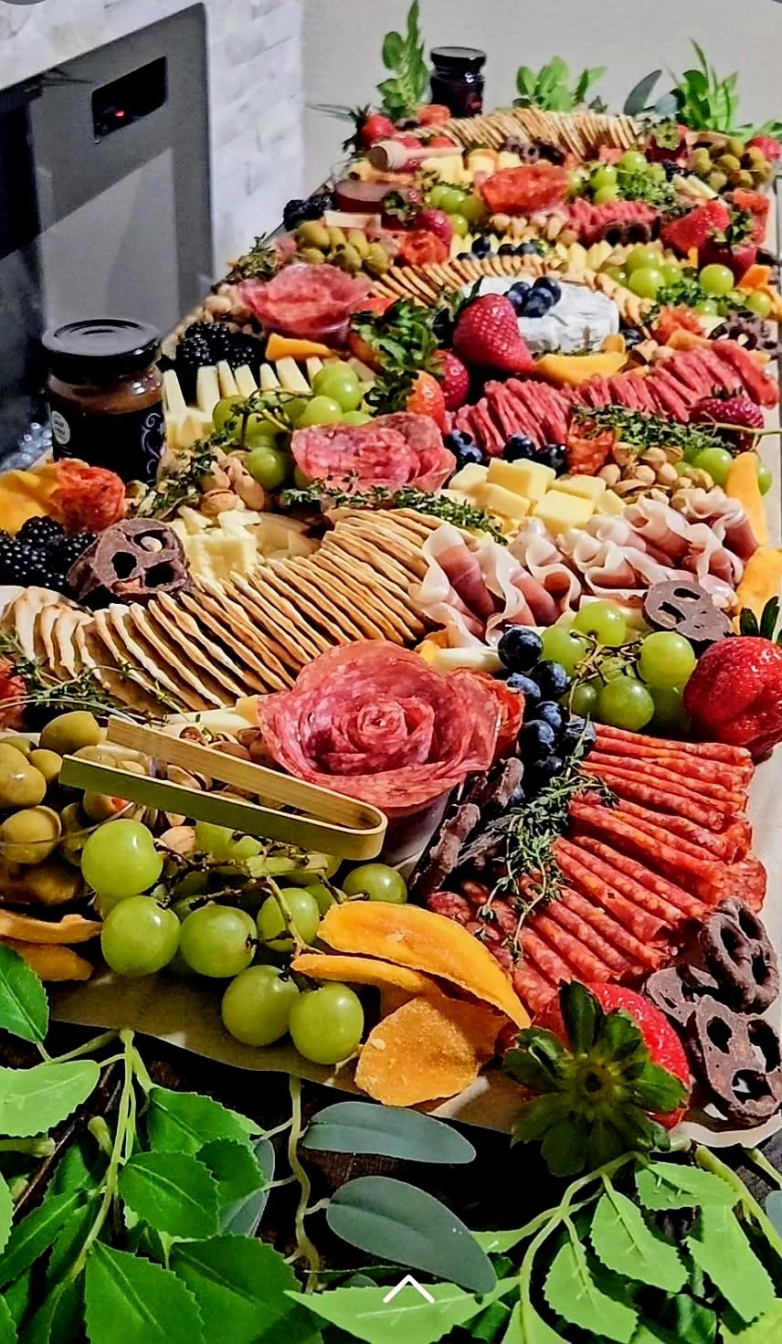 A large charcuterie and cheese platter with grapes, strawberries, sliced meats, cheeses, crackers, and garnishes.