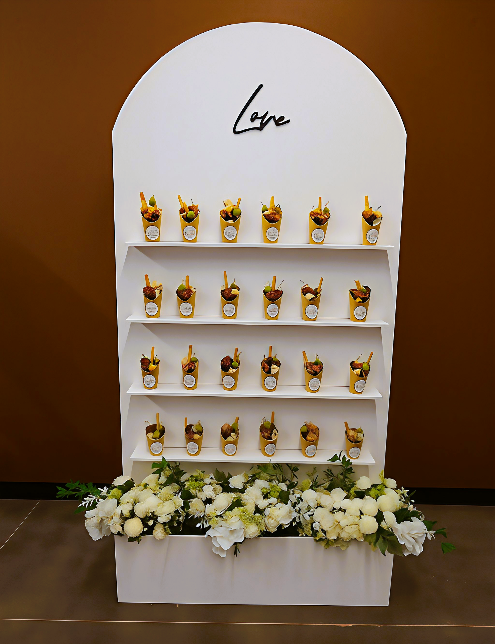 Display shelf with small decorative containers filled with food, arranged on four shelves, and a floral arrangement at the base. The word "Love" is written at the top.