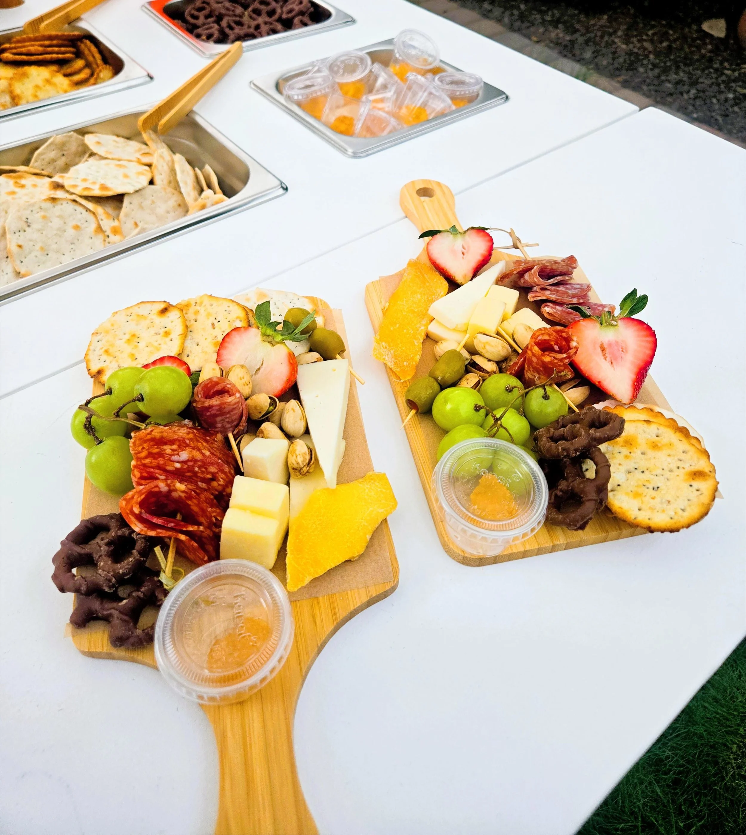 Cheese, strawberries, grapes, crackers, cured meats, nuts, and honey served on small wooden trays at an outdoor setting.