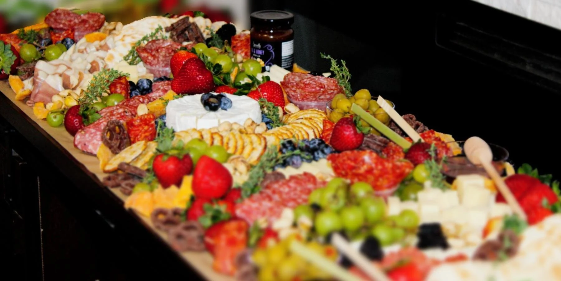 A cheese and charcuterie table with strawberries, grapes, blueberries, sliced meats, cheeses, and assorted crackers.