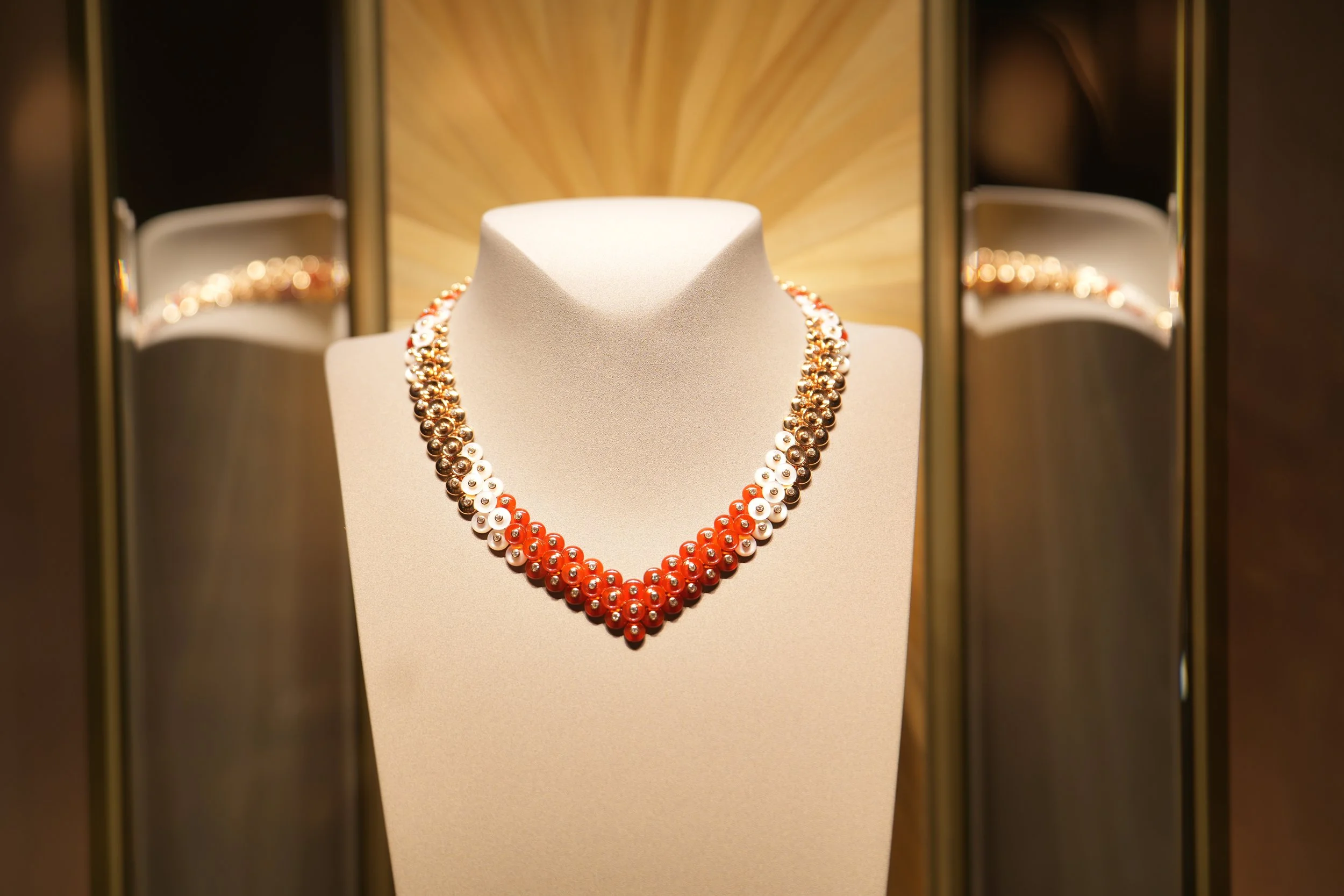 Colorful pearl necklace displayed on a jewelry bust in a jewelry store, with a warm background and reflection in the mirror.