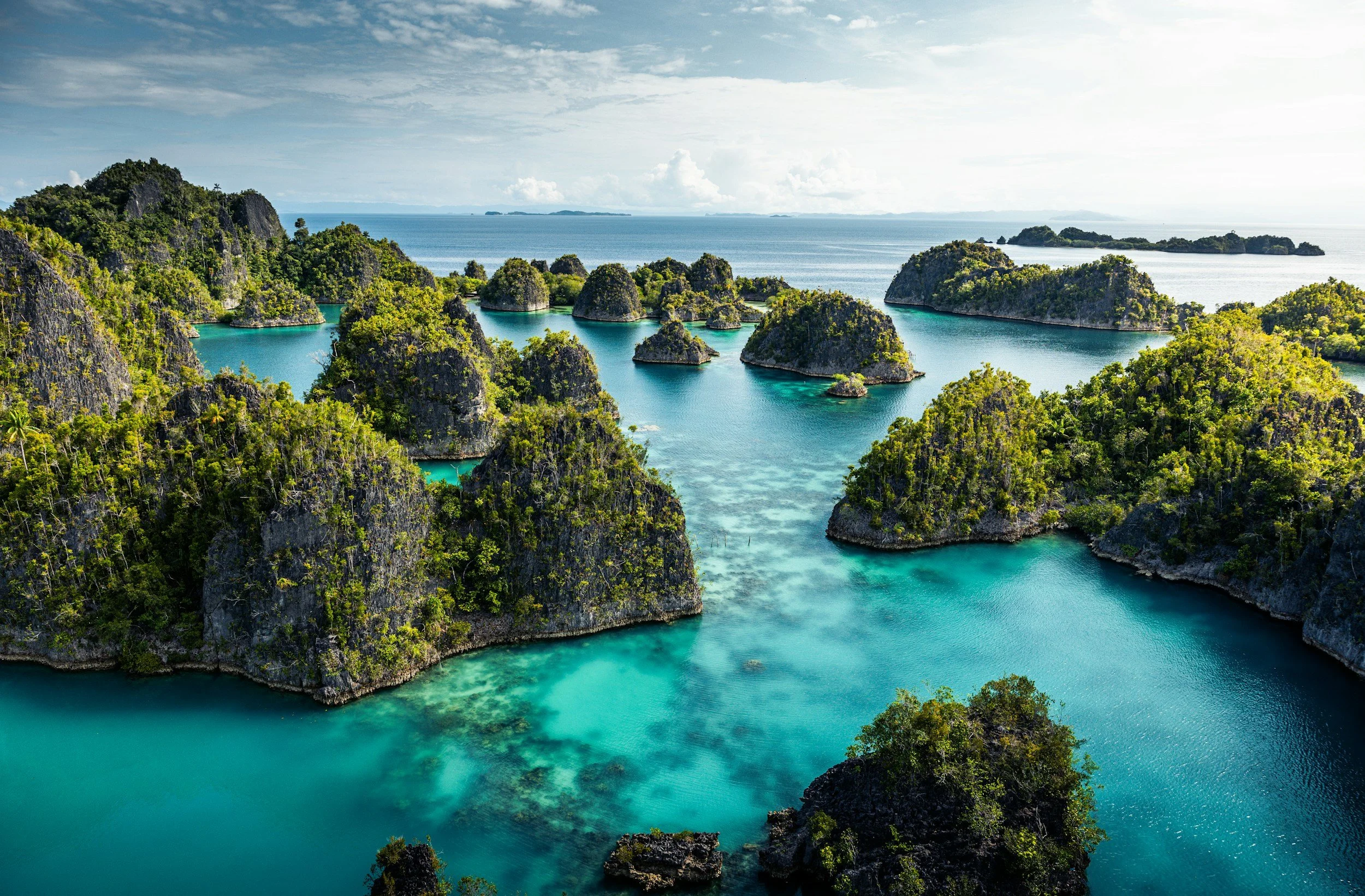 Tropical landscape with turquoise waters, lush green islands, and limestone cliffs under a partly cloudy sky.