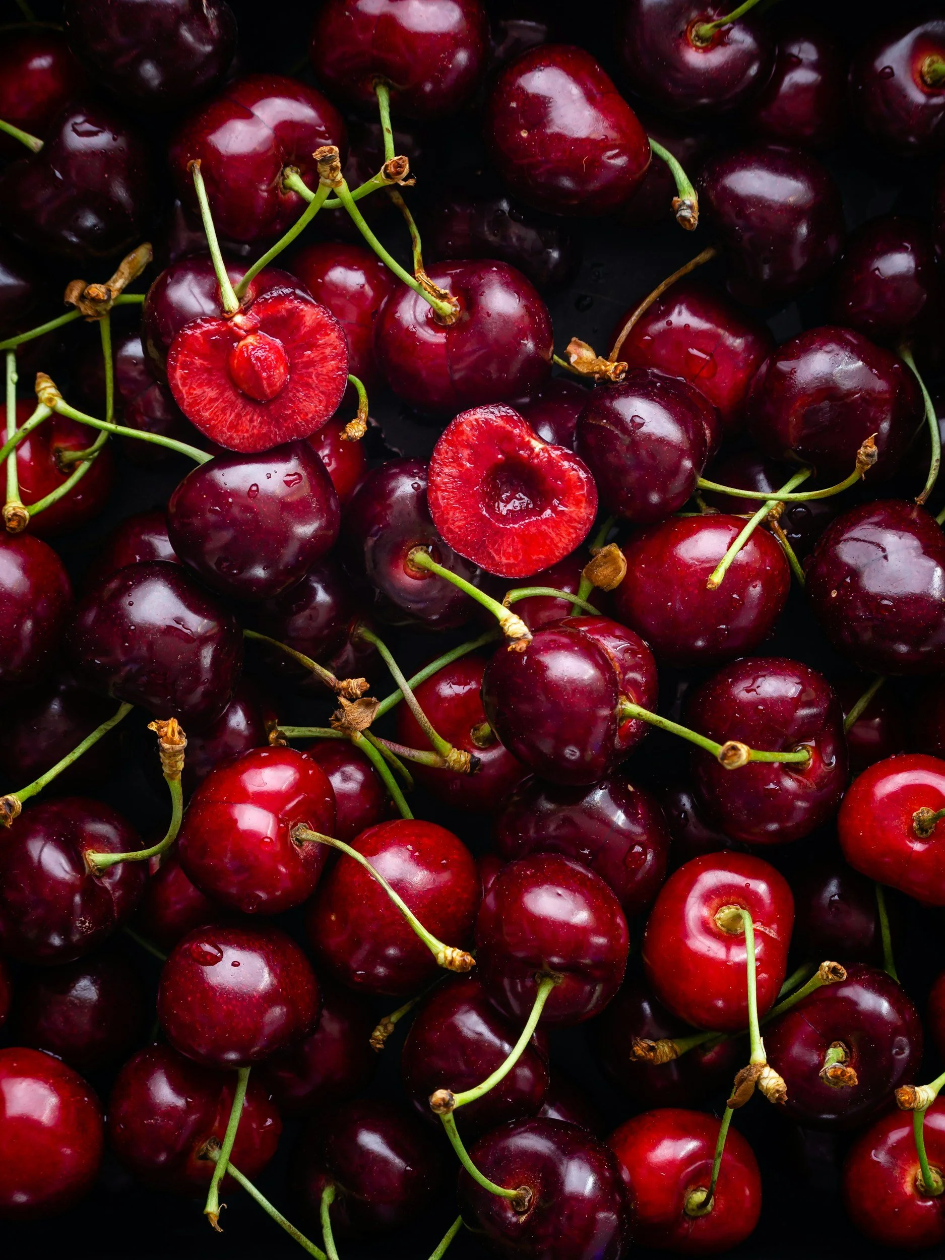 Fresh red cherries with some cut open to show the pits inside.