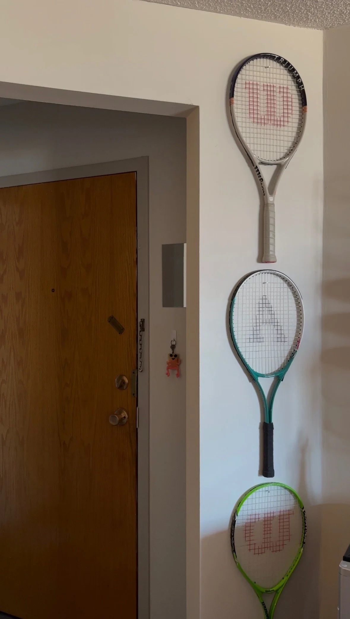 Three tennis rackets hanging vertically on a white wall near an entryway.