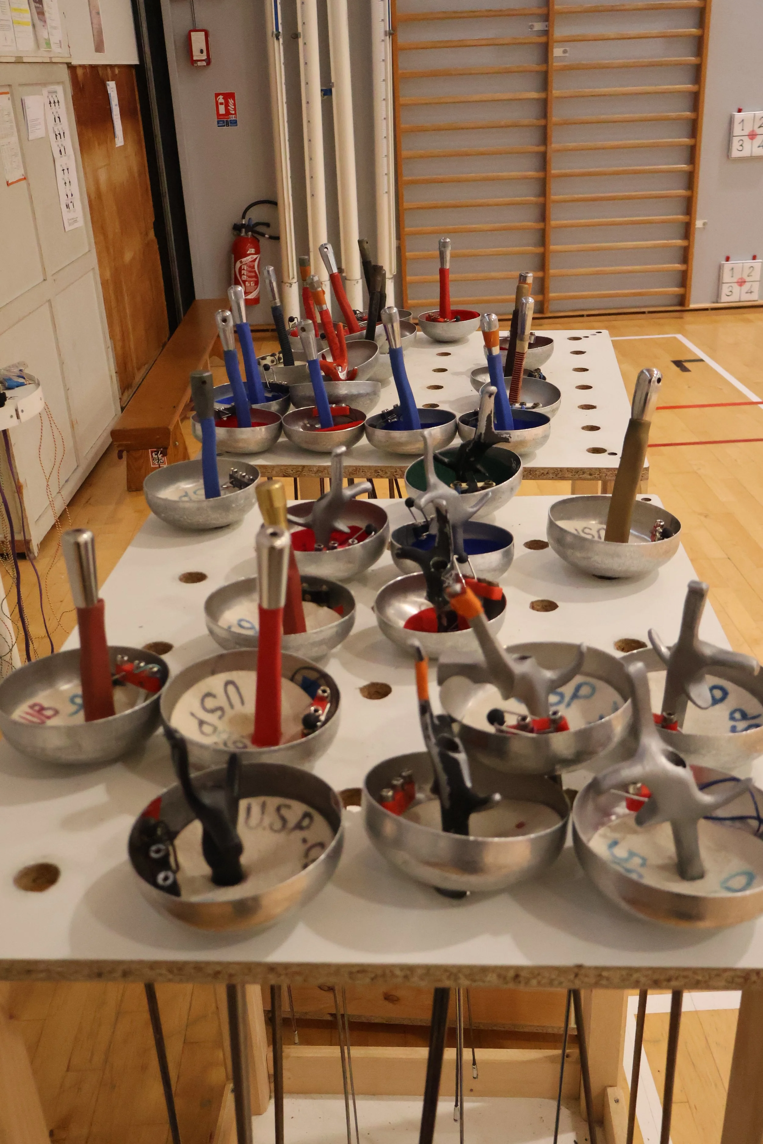 Une table avec plusieurs épées en métal, armes de l'escrime sportive, utilisée lors des séances d'escrime pour les enfants, les adolescent et les adultes dans un gymnase adaptée à la pratique de l'escrime à l'electrique.