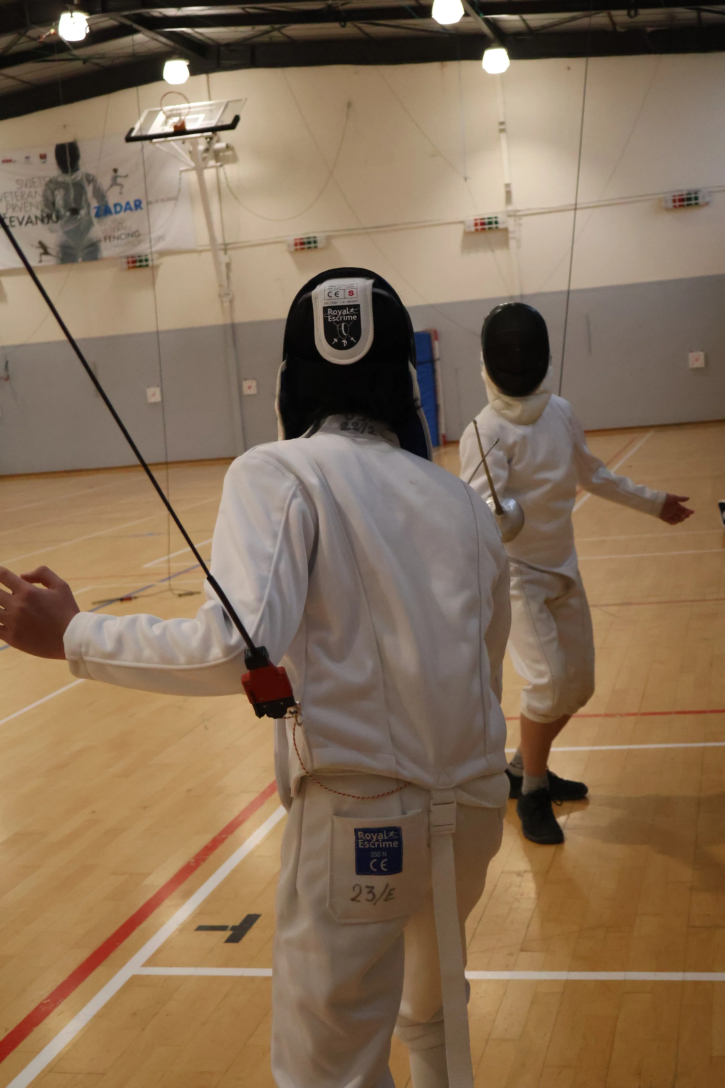 Jeunes adolescents pratiquant l'escrime dans un gymnase, portant l'équipement de protection.