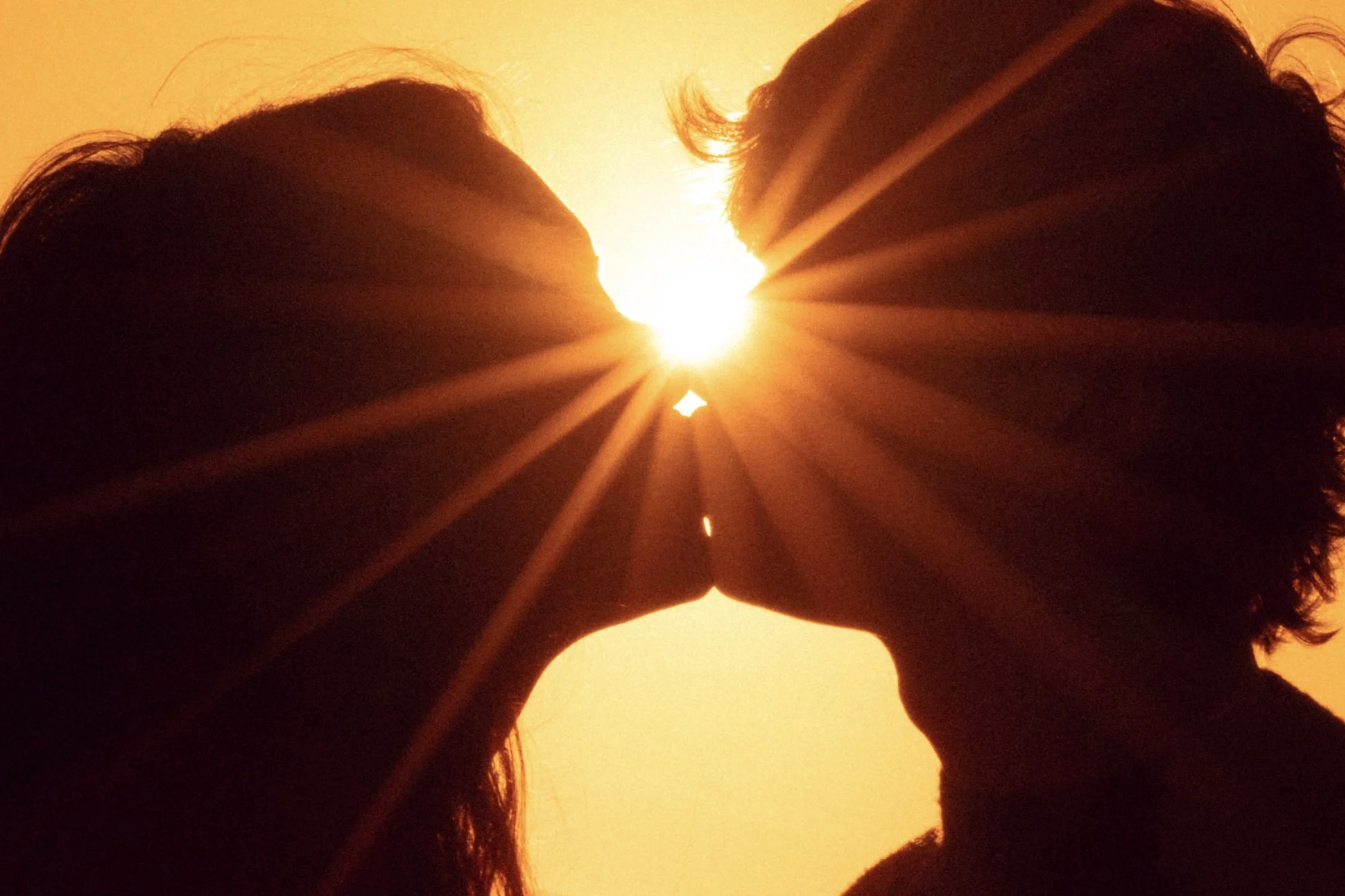 Silhouettes of two children facing each other at sunset with the sun between them.