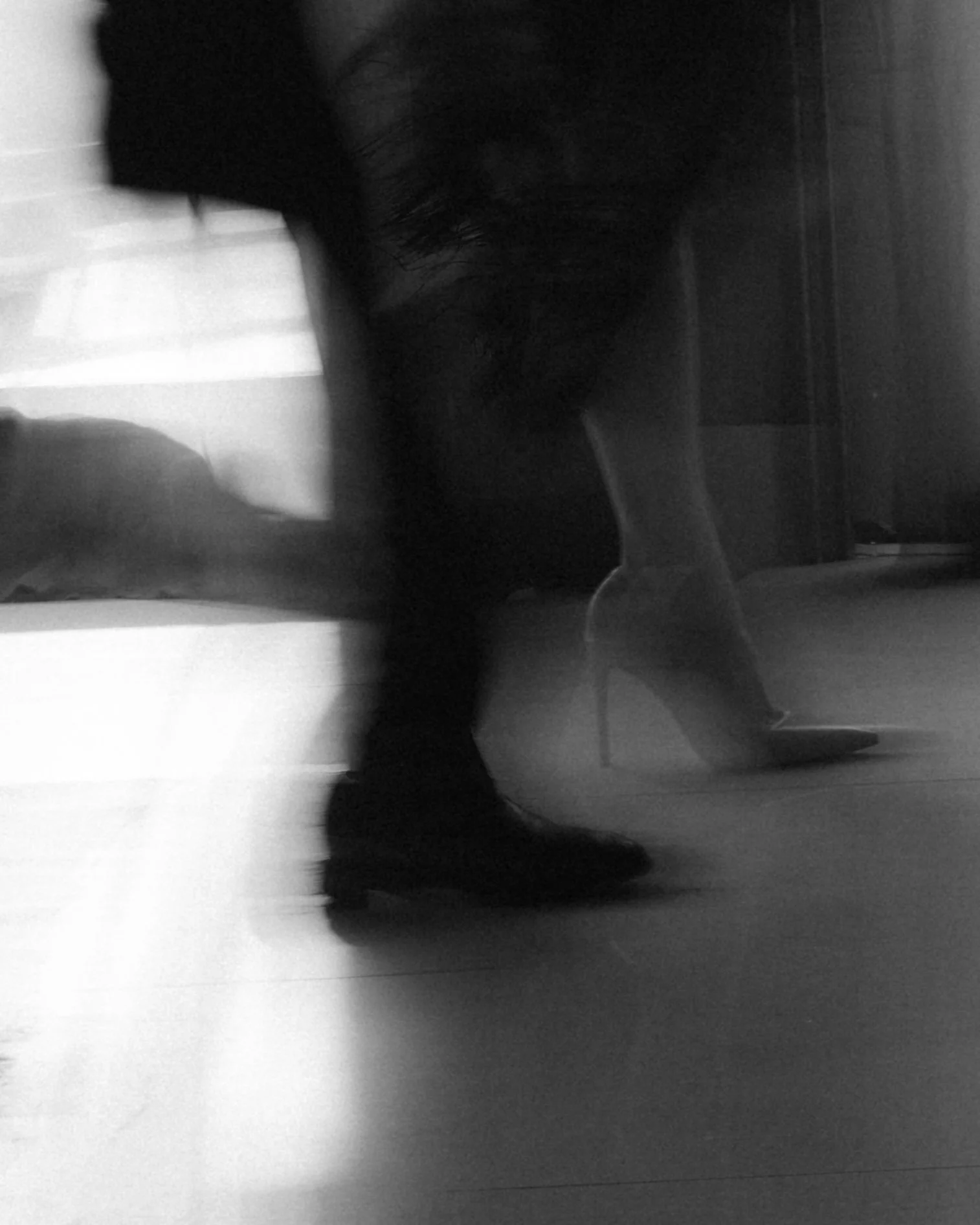 A rear view of a person wearing dark clothing and high heels, walking in an indoor space with smooth flooring and partition walls.