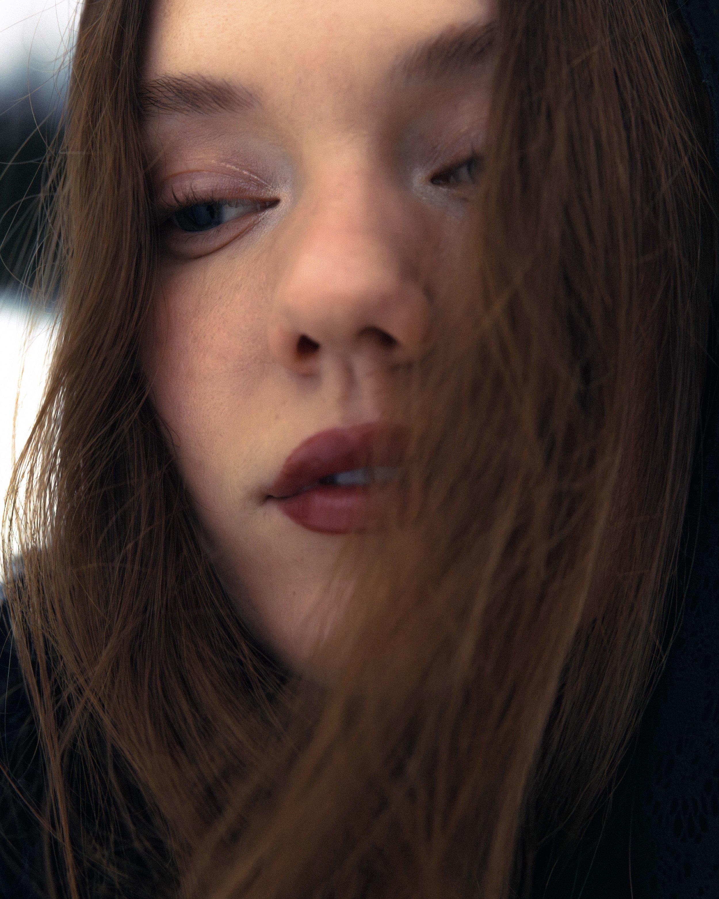 Close-up of a woman's face with long brown hair, one eye partially closed, and soft makeup.