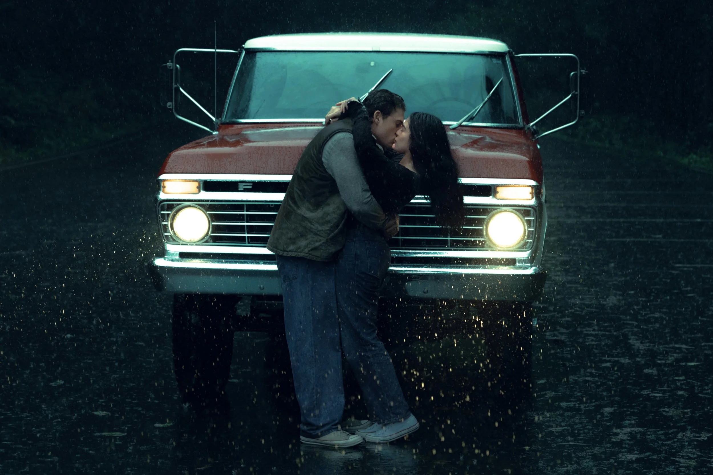 A couple kissing in the rain in front of a red vintage van.