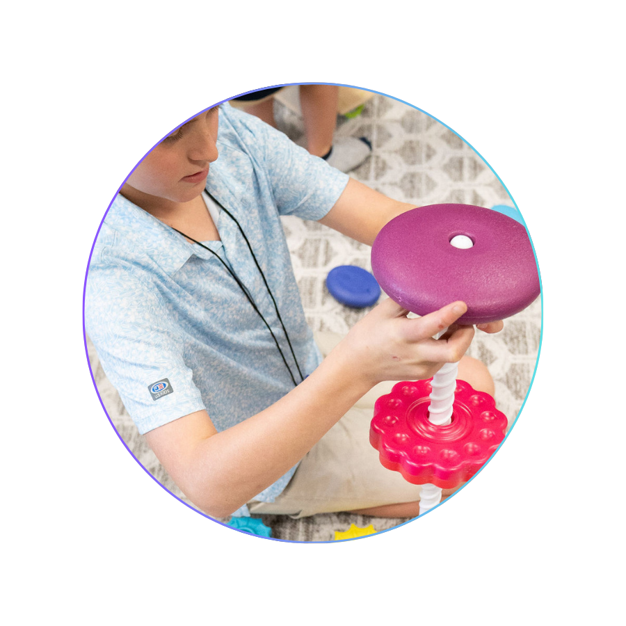 A young boy sitting on a patterned carpet playing with a vertical spinning toy with purple and red discs.