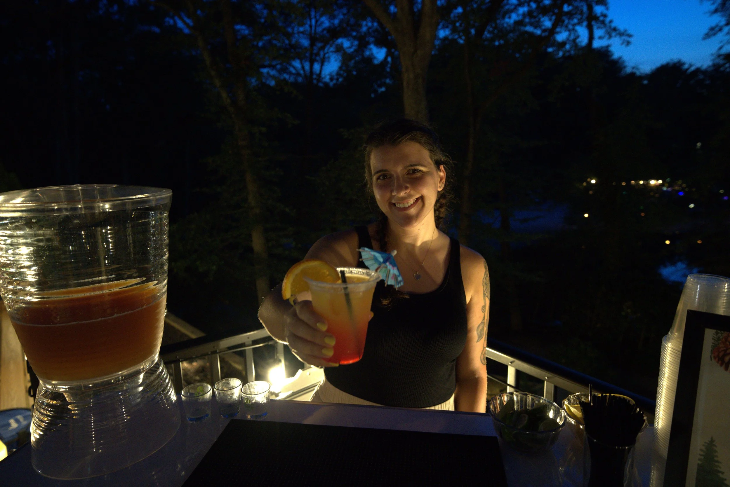 the owner, Cara, holding up a cocktail behind the bar and smiling