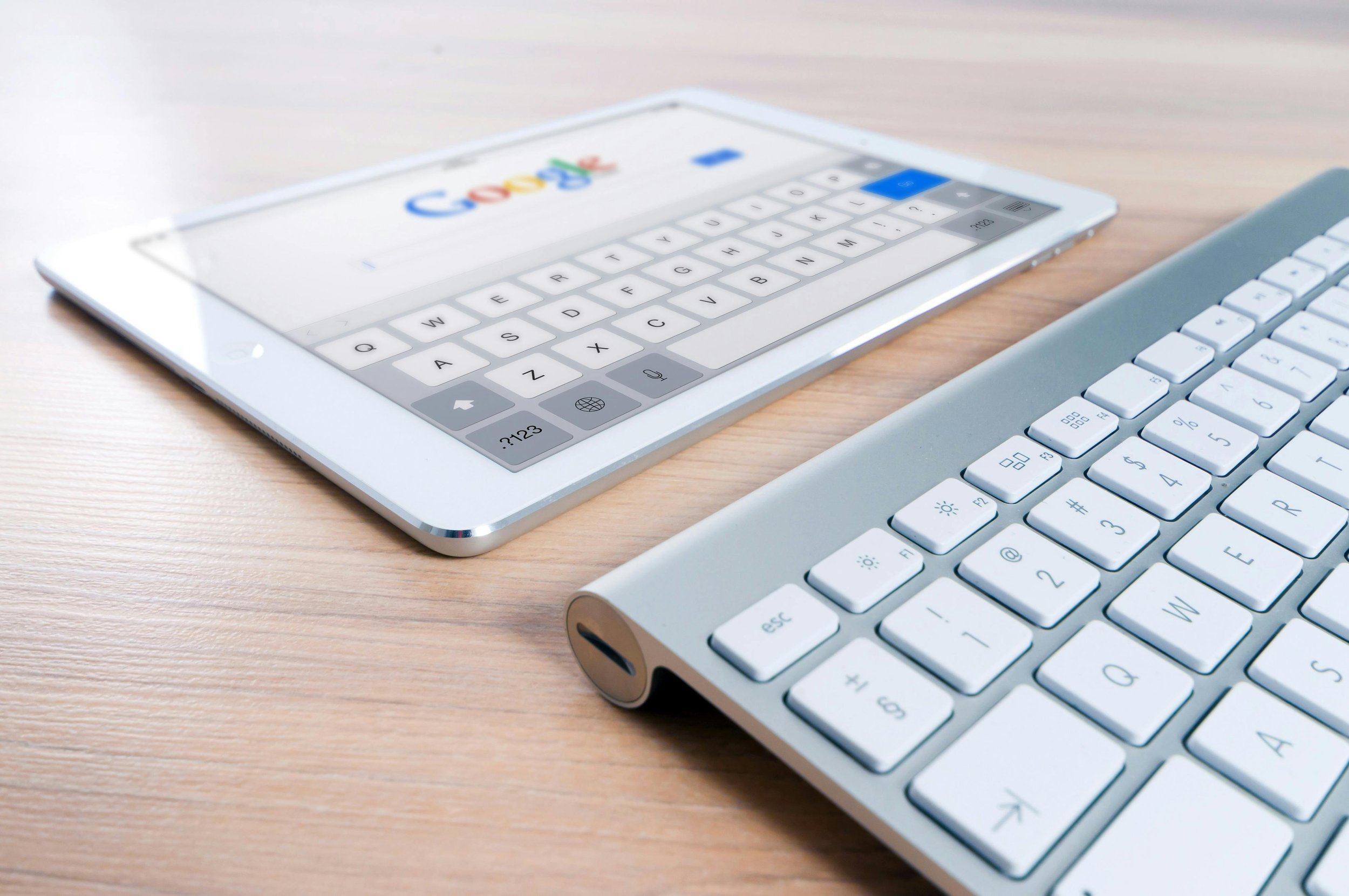 White tablet displaying Google search page and a white keyboard on a wooden desk.