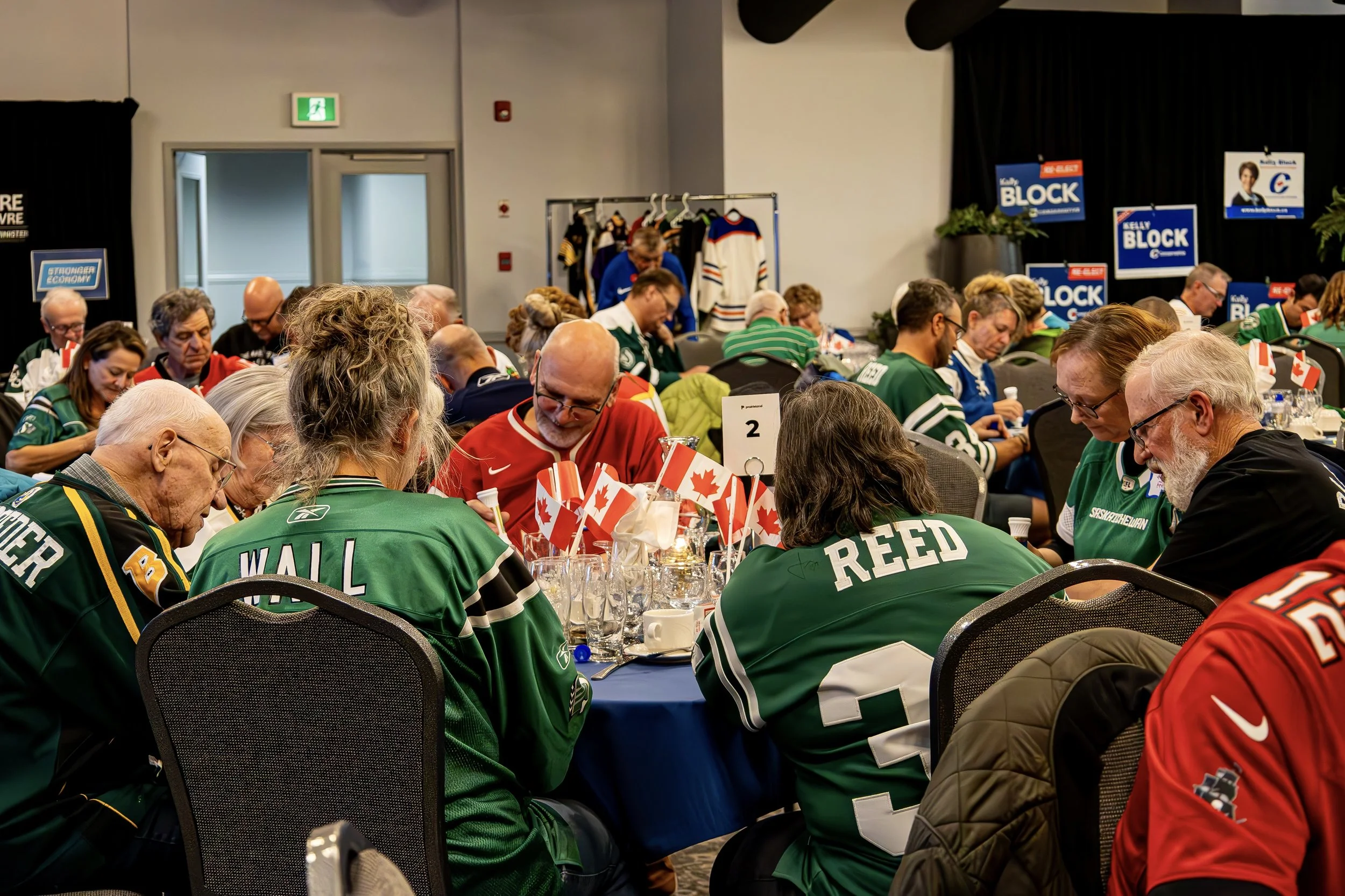 People wearing hockey jerseys seated at a banquet table with Canadian flags and beverages, participating in an event.