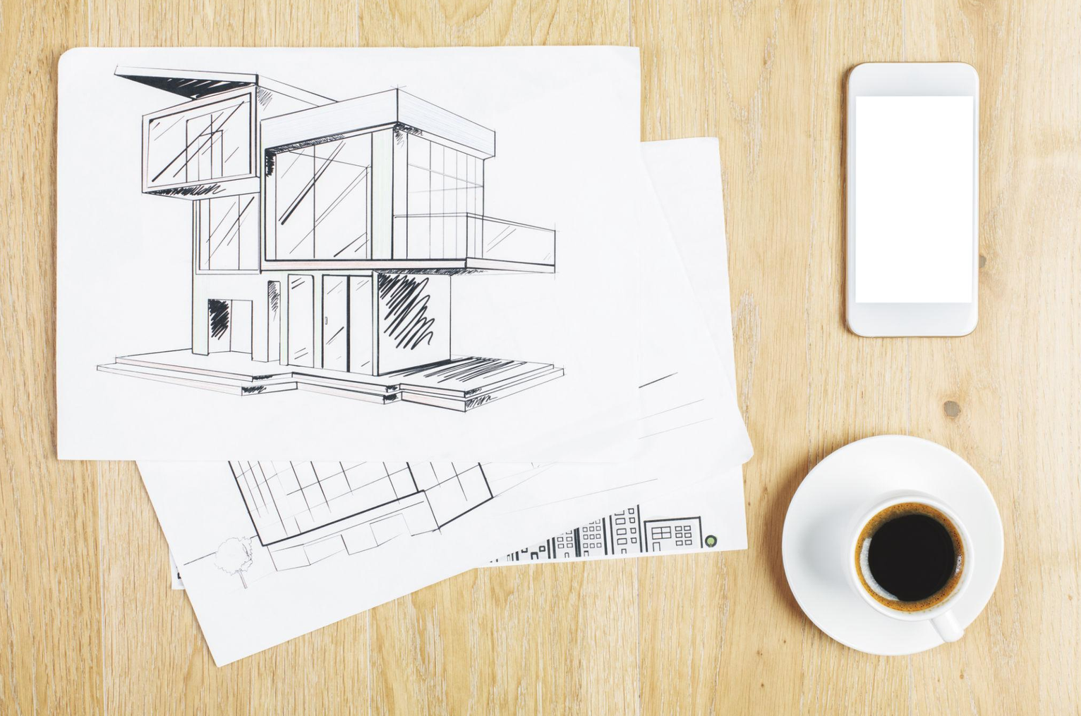 Architectural sketches of a modern building on white papers, placed on a wooden table with a smartphone, a cup of coffee, and a saucer.
