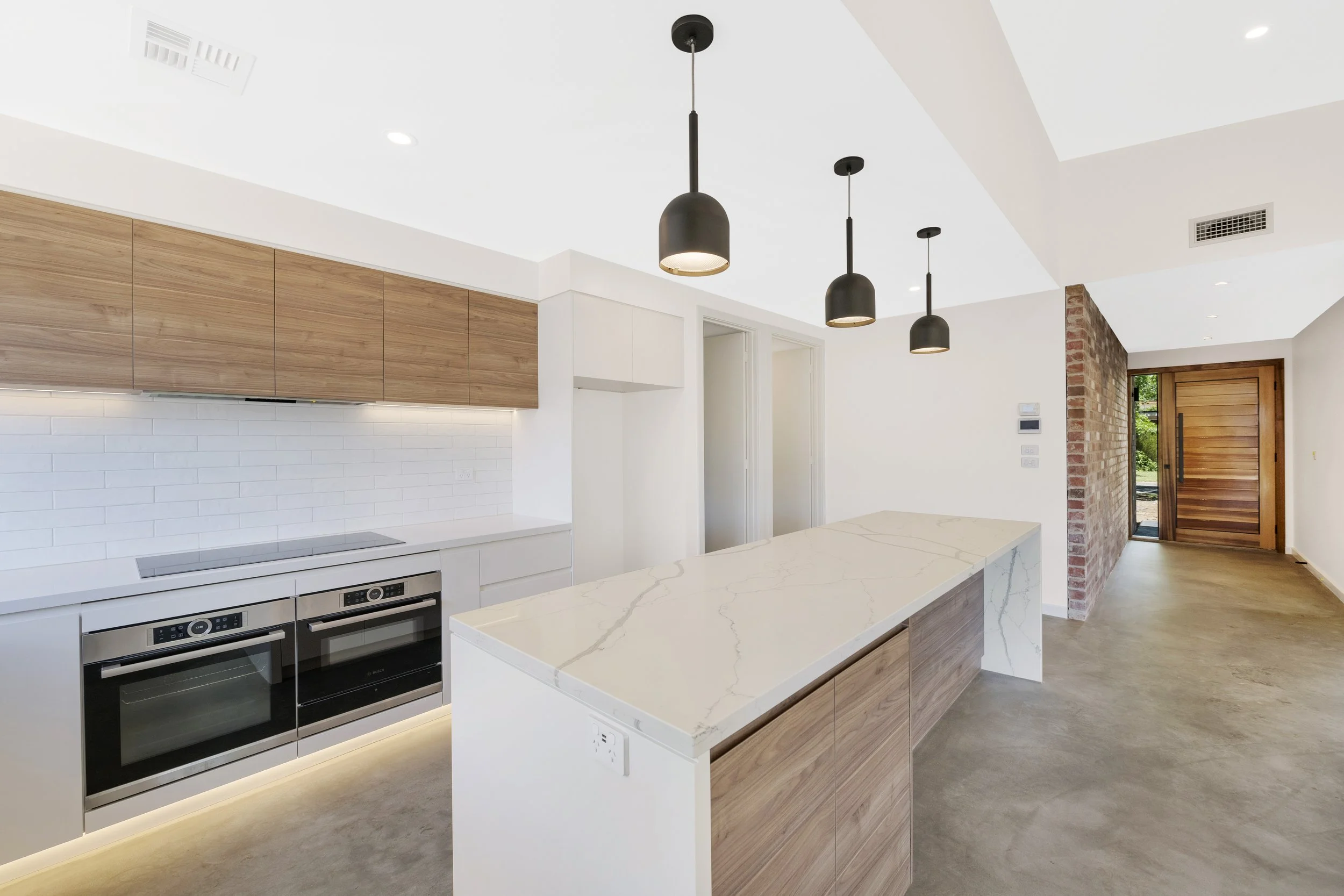 Light-filled modern kitchen with natural brickwork, timber finishes and an airy open-plan design by New Age Design Services