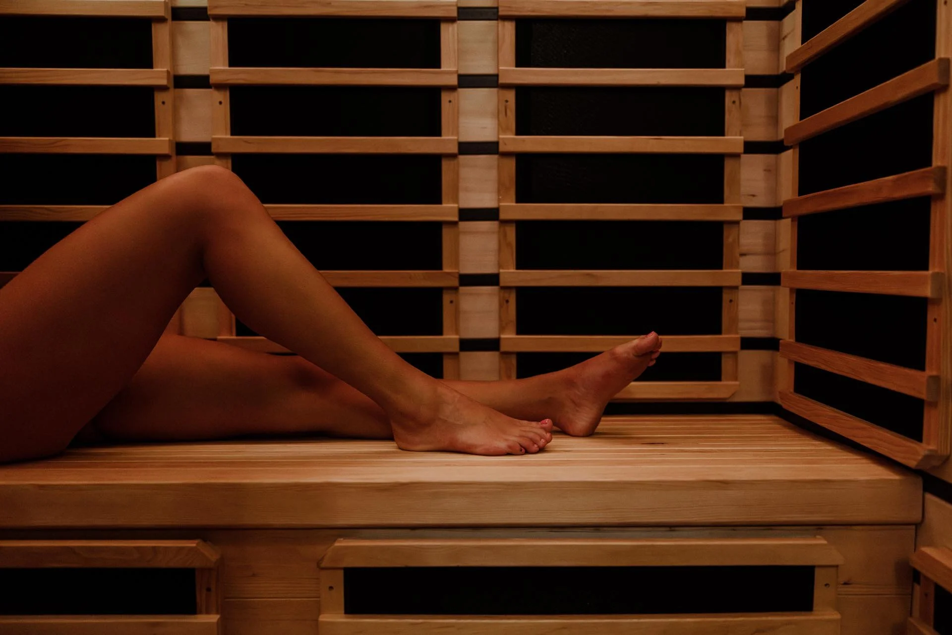 A person lying inside a wooden sauna, with their legs crossed and resting on the bench.