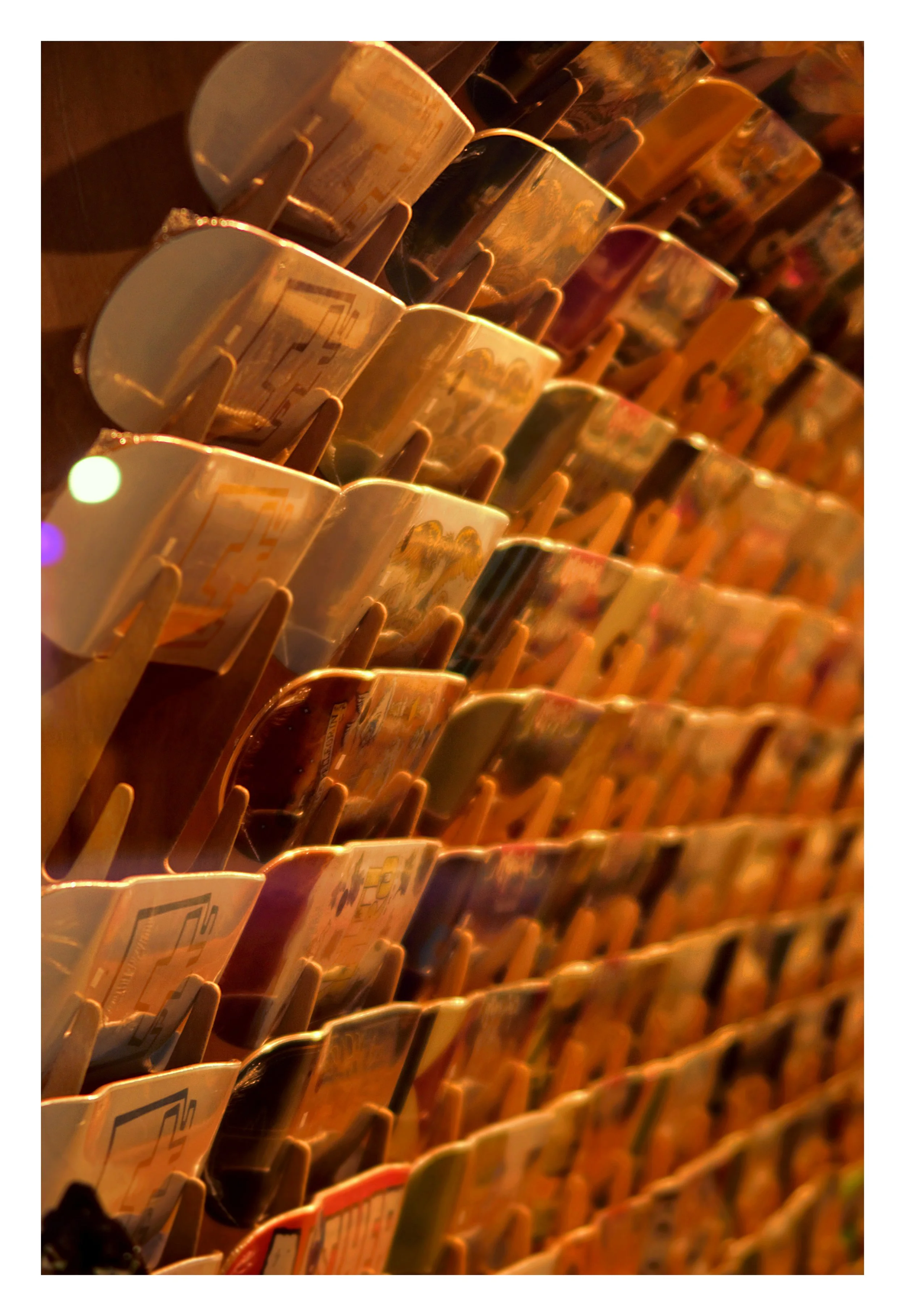 A display of multiple cups with vintage-style cityscape artwork, arranged in rows on wooden shelves, illuminated by warm lighting.