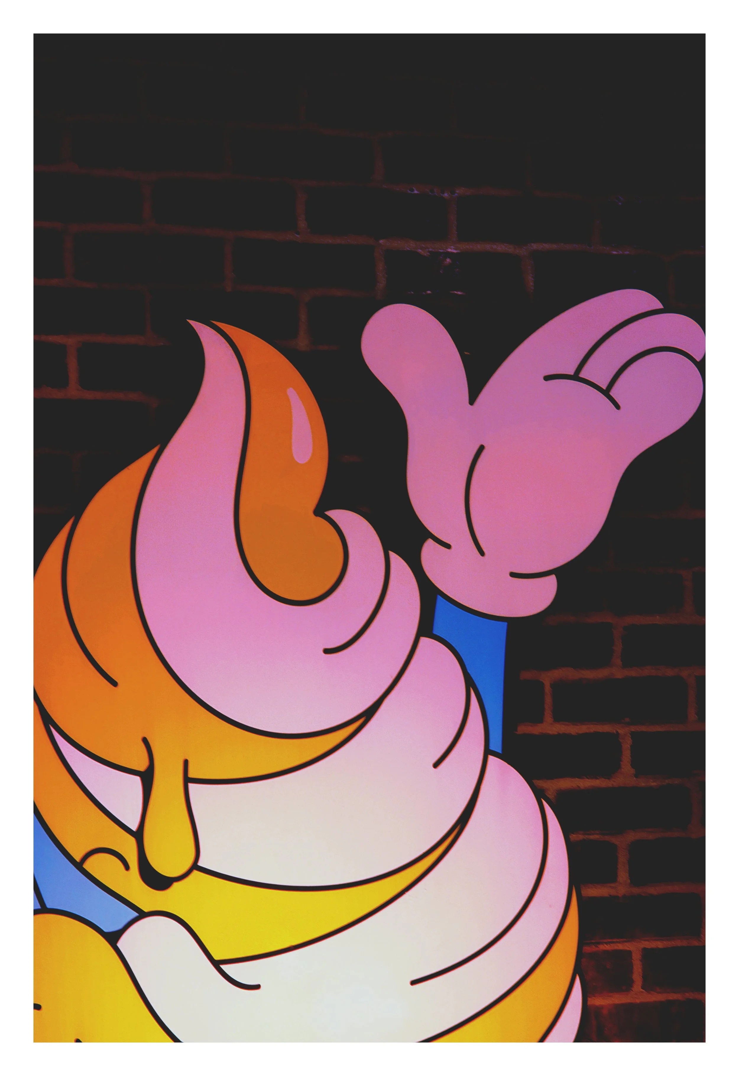 Close-up of a colorful cartoon wall art depicting a pink hand with a thumb and finger pointing upward against a dark brick wall background.