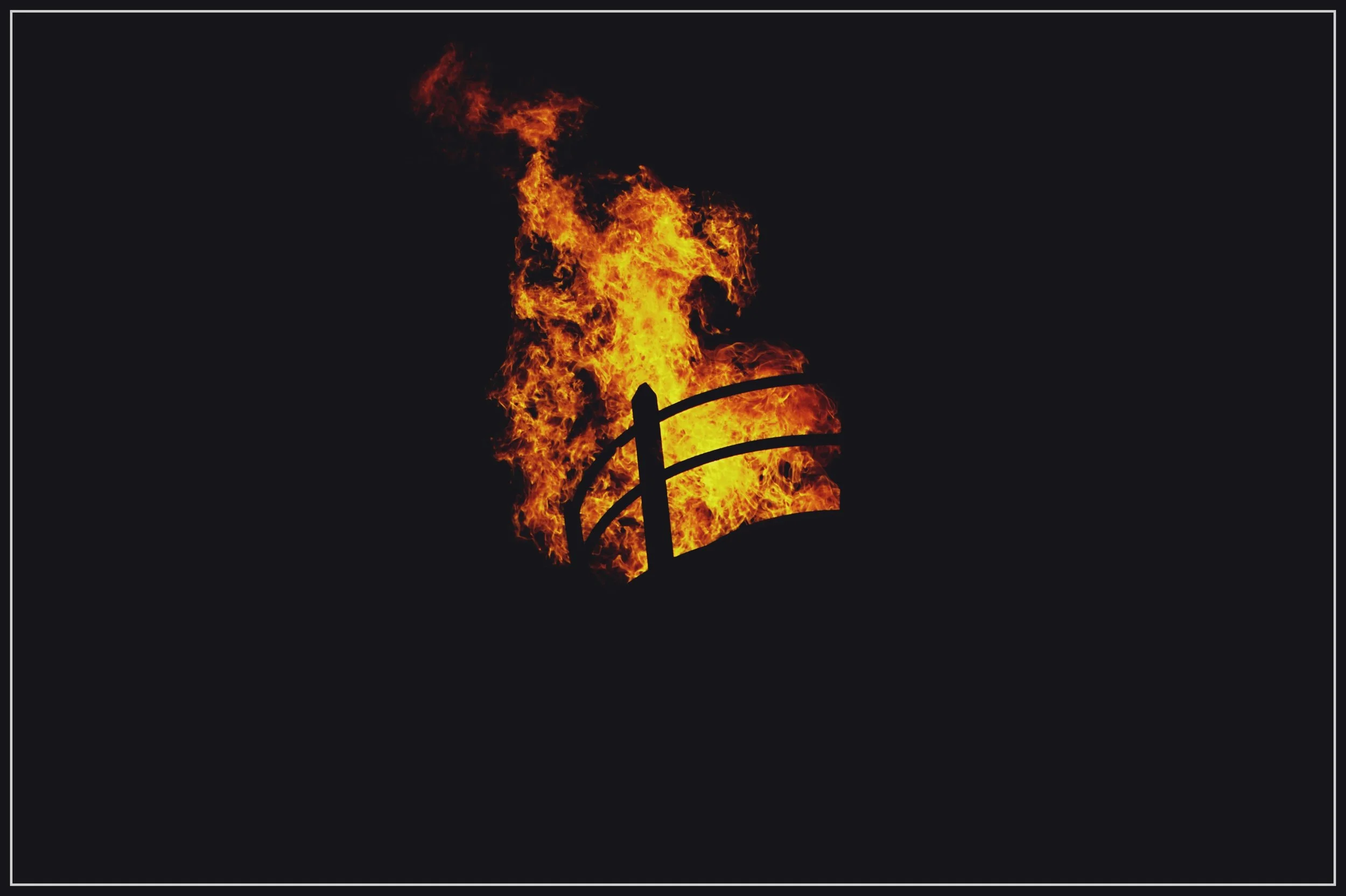 Fire engulfing a railing or fence in the darkness.