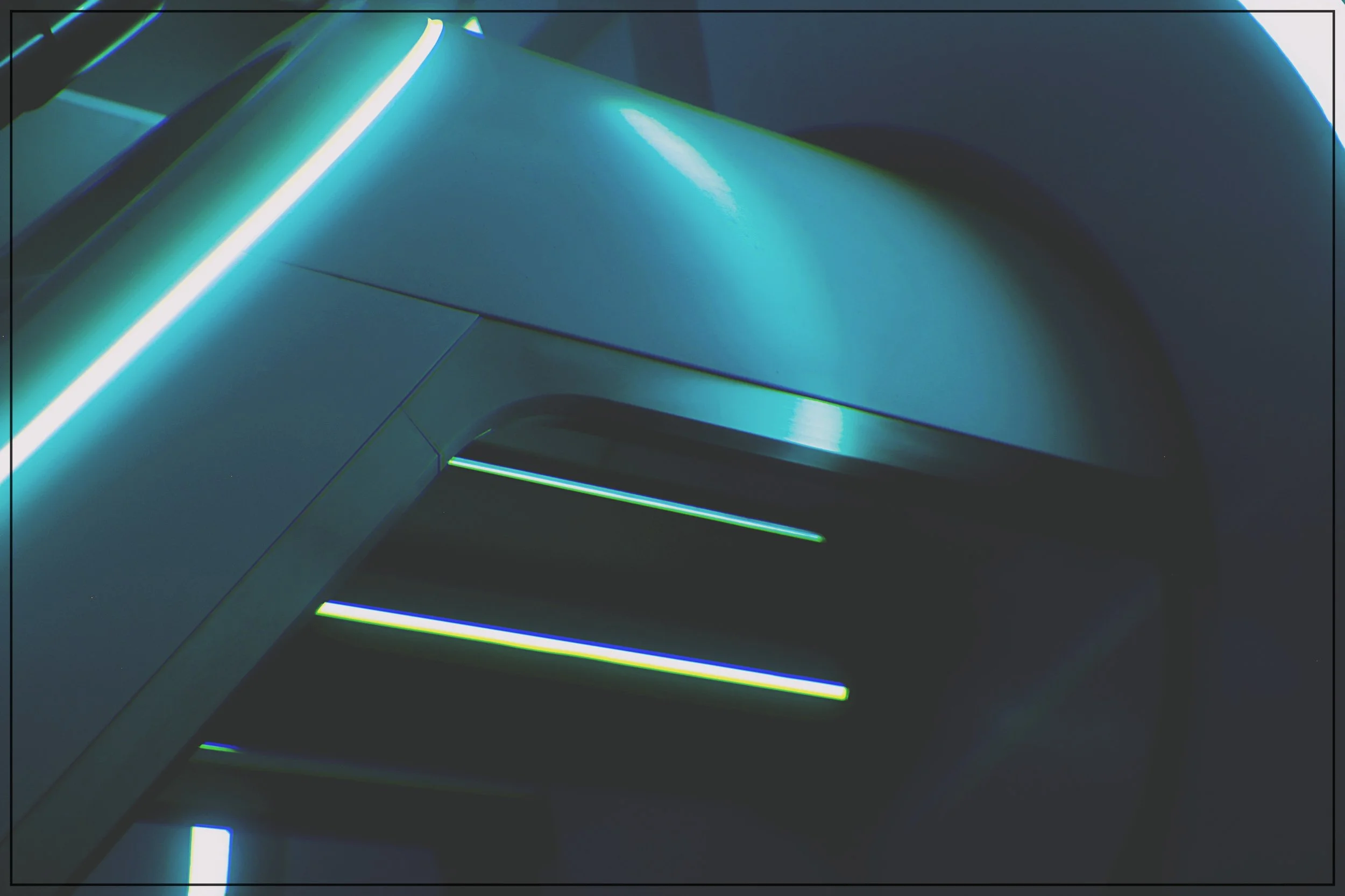 Close-up of a modern, sleek metallic structure illuminated by neon blue and green lights, possibly part of a futuristic installation or vehicle.