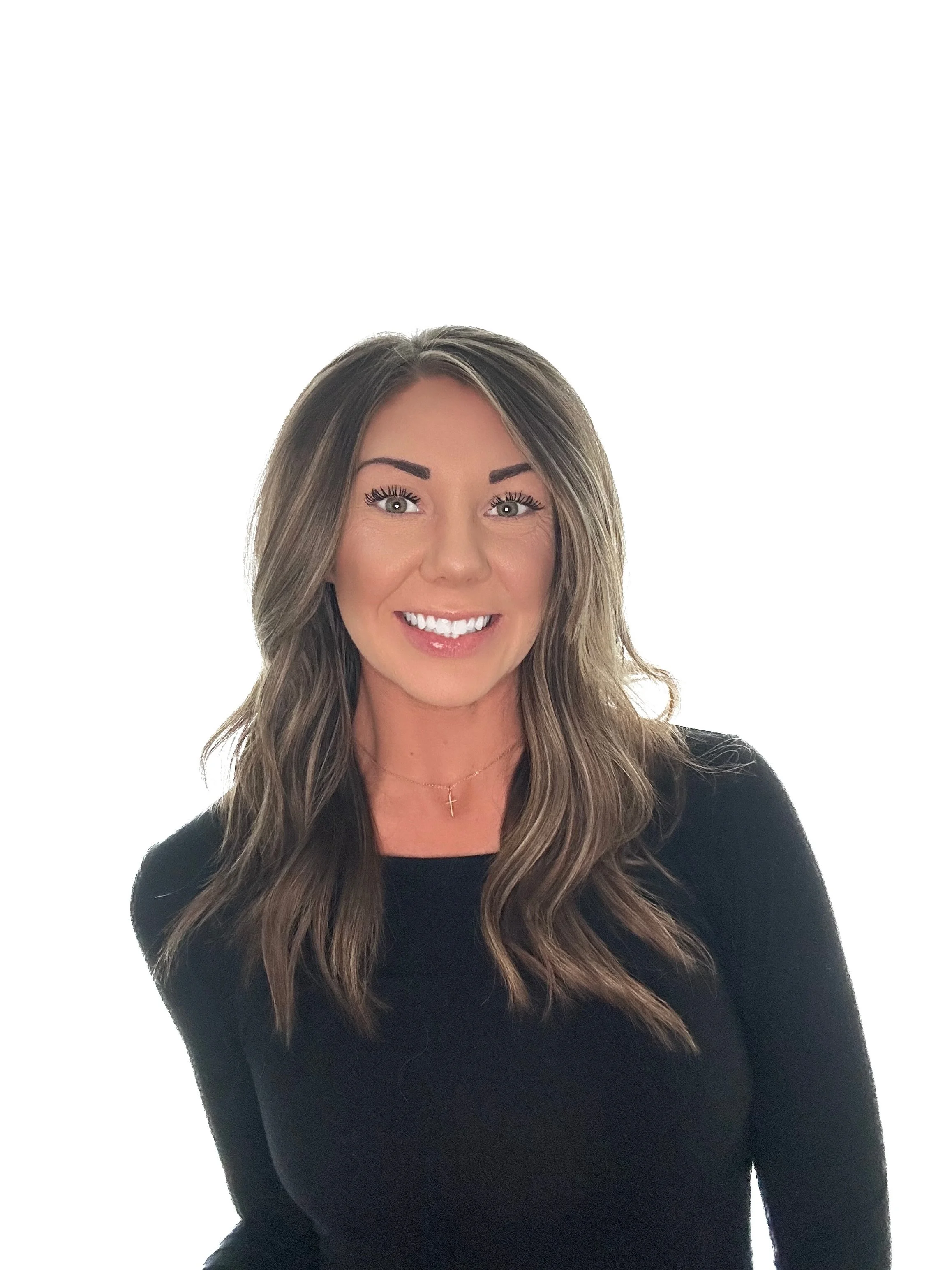 A woman smiling with long, wavy brown hair, wearing a black top and a small gold cross necklace.