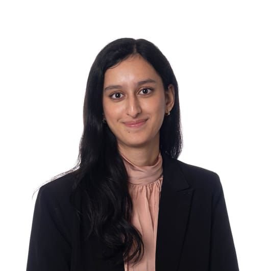 A woman with long dark hair wearing a black blazer and pink blouse against a white background.