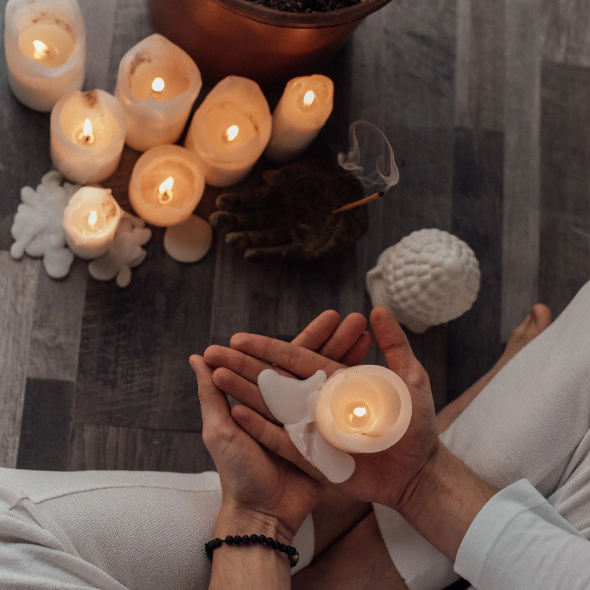 Hands holding a candle with candles below them on the floor representing Distance Reiki & Remote Energy Healing Sessions.