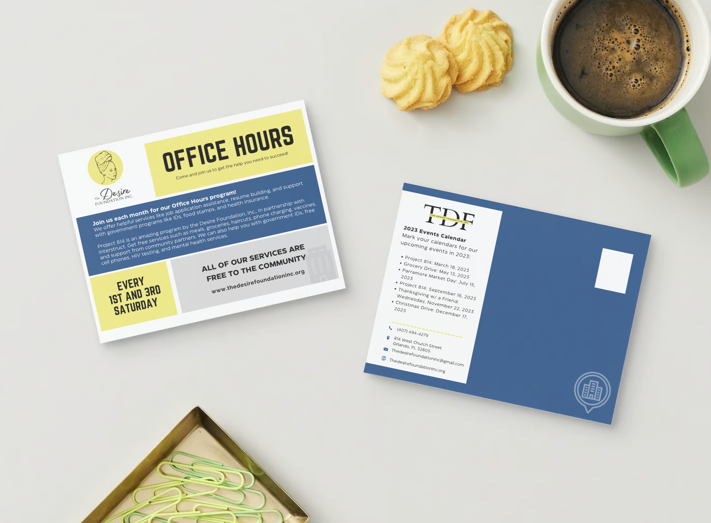 Flyers on a white desk, one promoting office hours and community services, the other listing 2023 events calendar, next to a cup of coffee, cookies, and a box of paper clips.