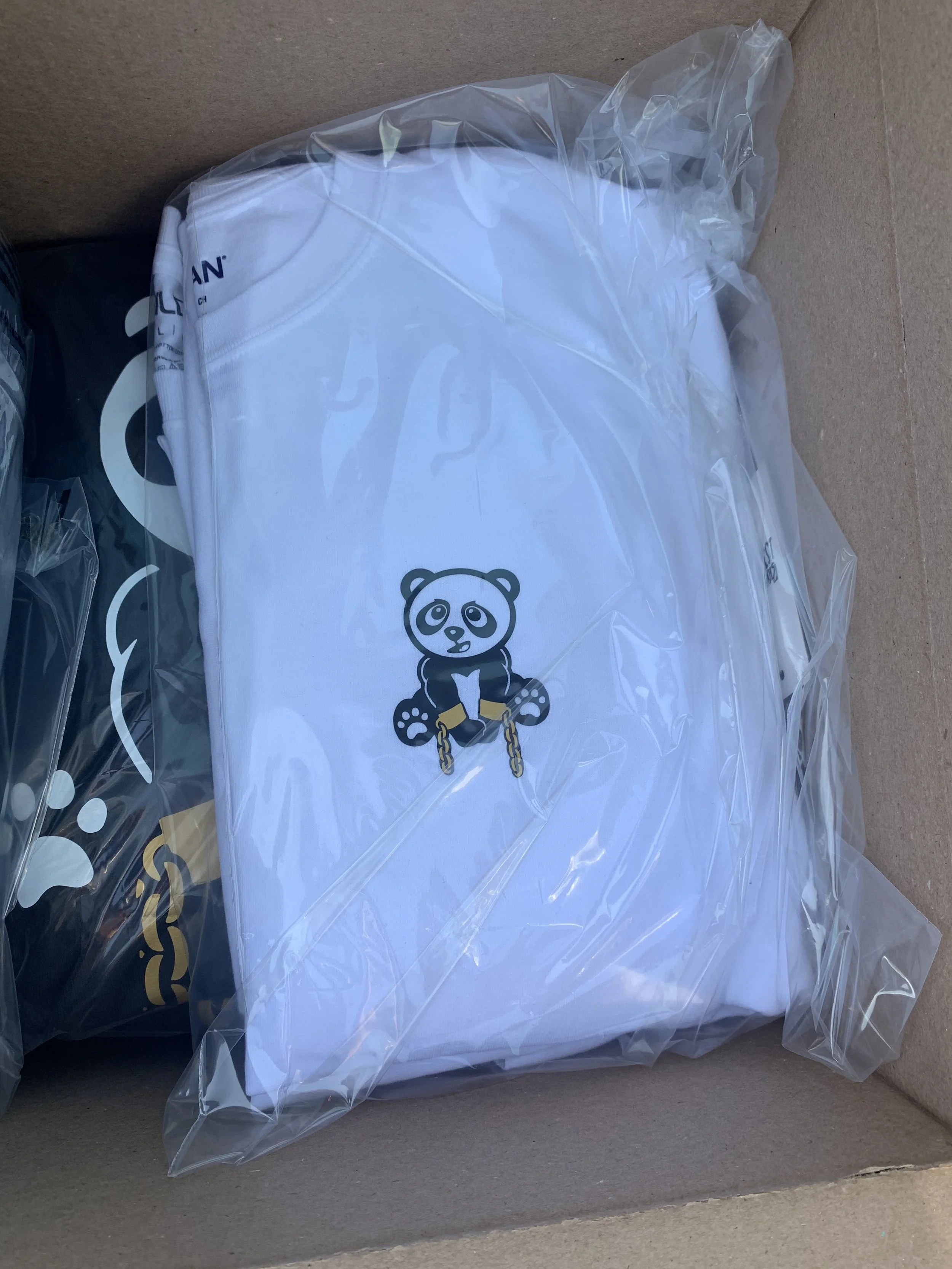White folded clothing with a panda bear logo, inside a clear plastic bag, placed in a cardboard box.