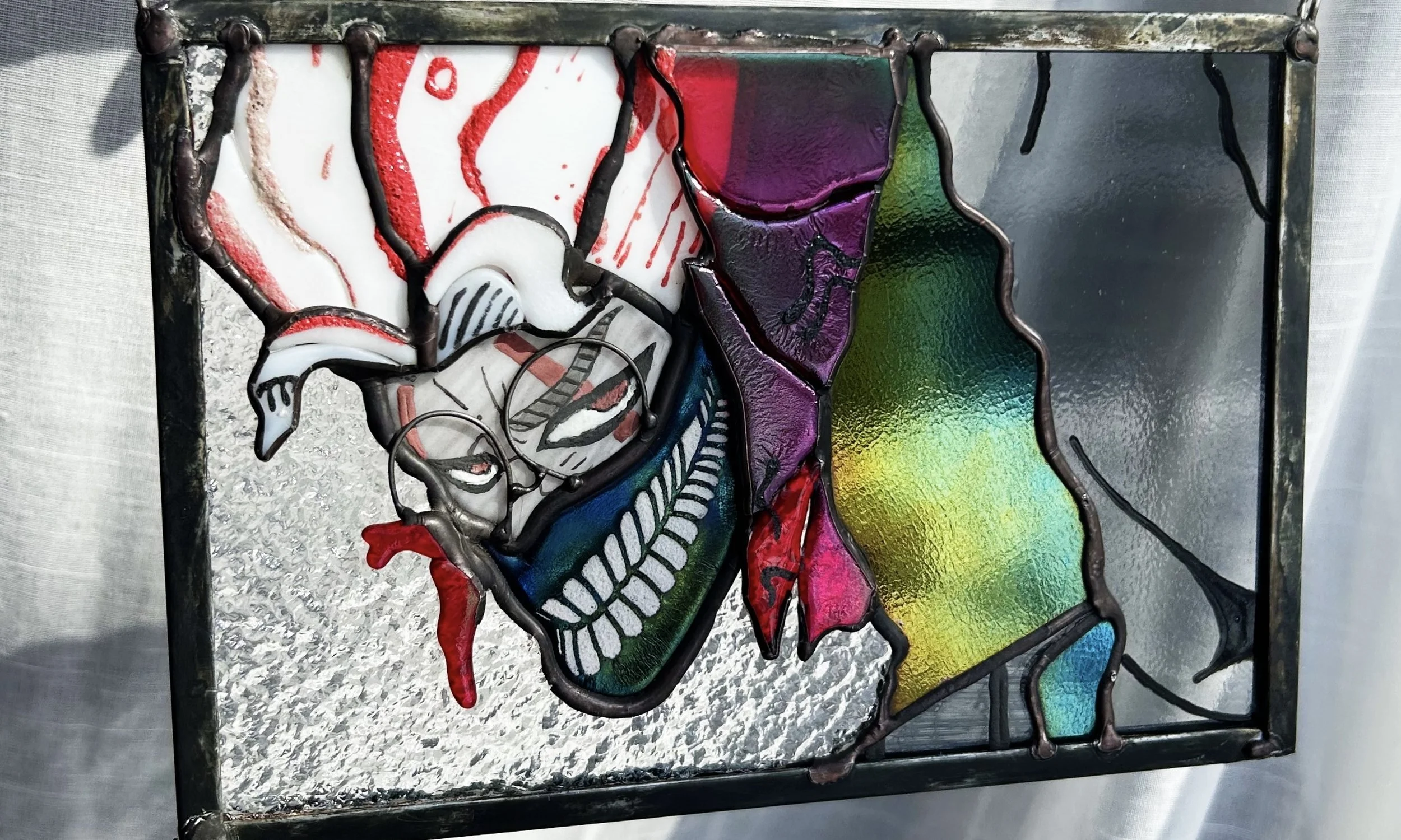 Abstract stained glass artwork featuring Okarun from the anime and manga DANDADAN using various colors and shapes, including a  red, white, black, purple, and iridescent sections, framed by a dark metal border.
