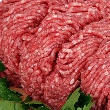 Close-up of raw ground beef patties with herbs underneath.