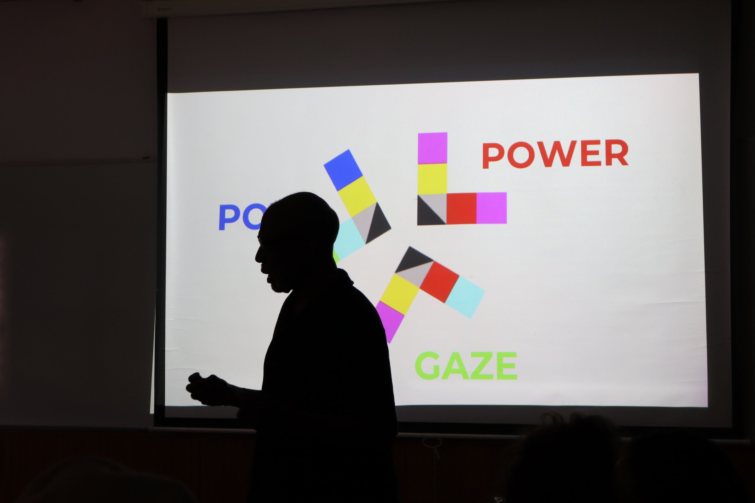 Silhouette of a man standing in front of a presentation slide with colorful geometric shapes and the words 'POWER', 'GAZE', and 'POWER' in red, green, and blue text in a film workshop in Lisbon.