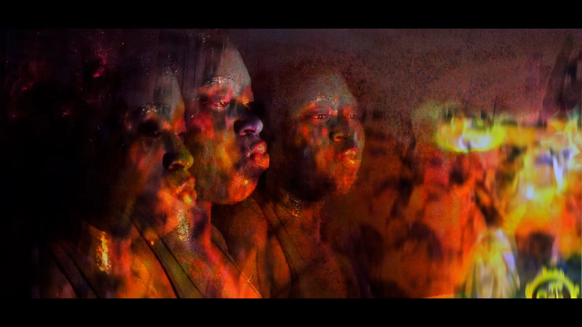 Multiple women with painted faces and closed eyes, standing in a row against a dark background with fiery, glowing colors.