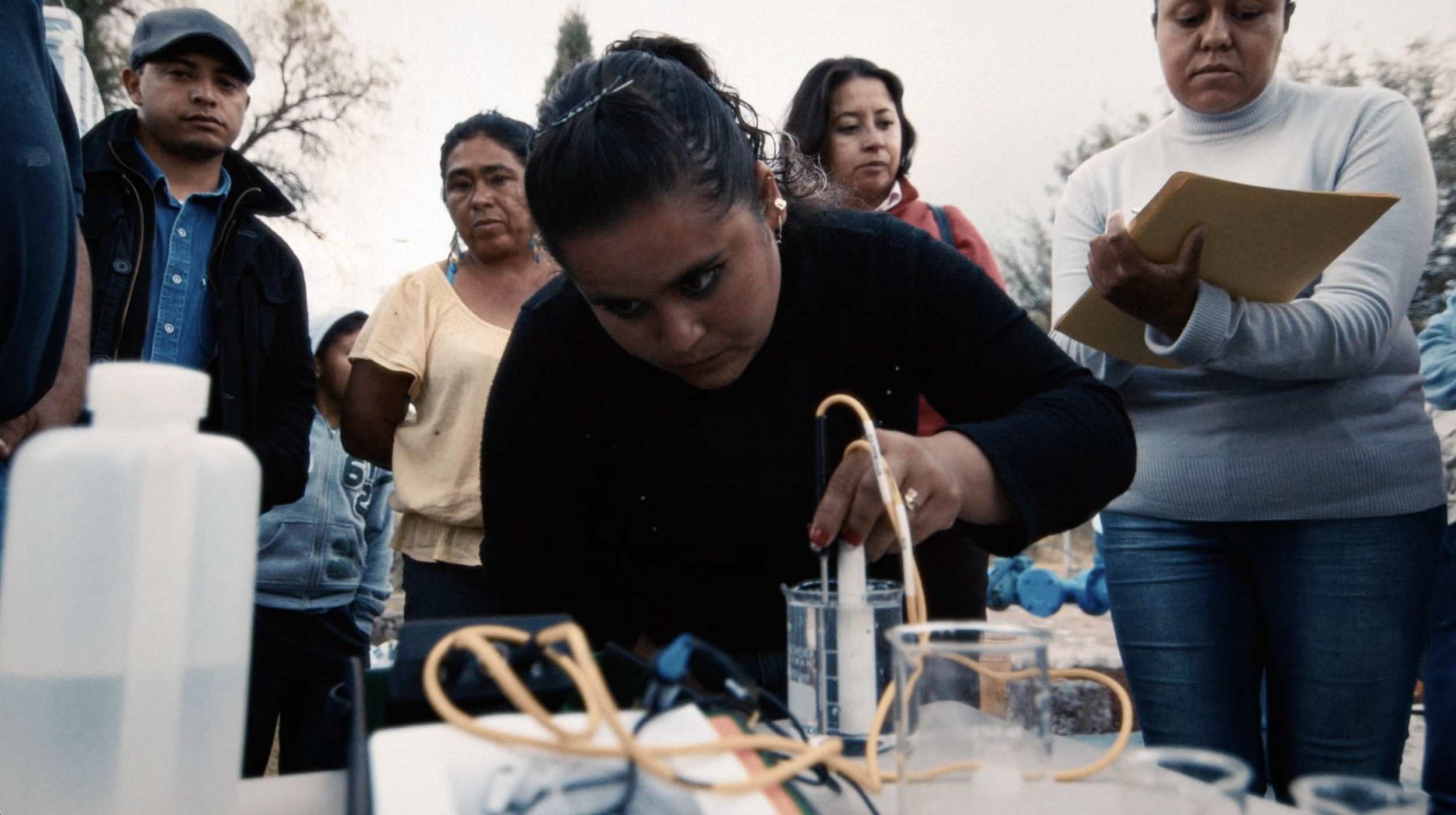 Woman conducting a science experiment outdoors while surrounded by onlookers.