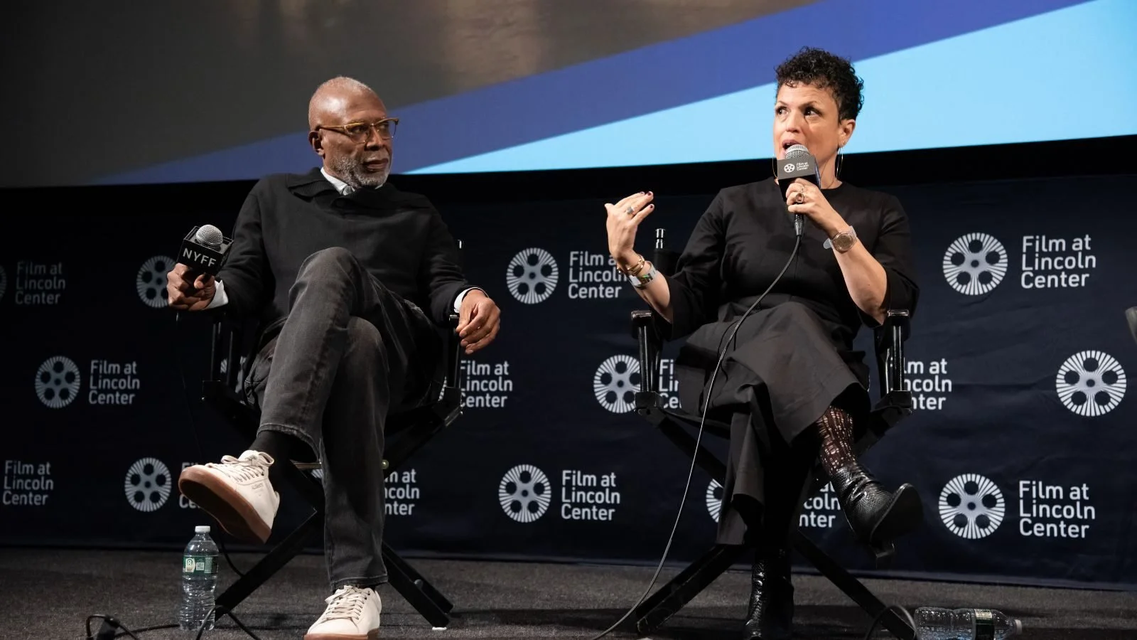 Two people speaking on stage at the Lincoln Center, with microphones in hand, having a conversation during an event, with a backdrop displaying 'Film at Lincoln Center' logos.