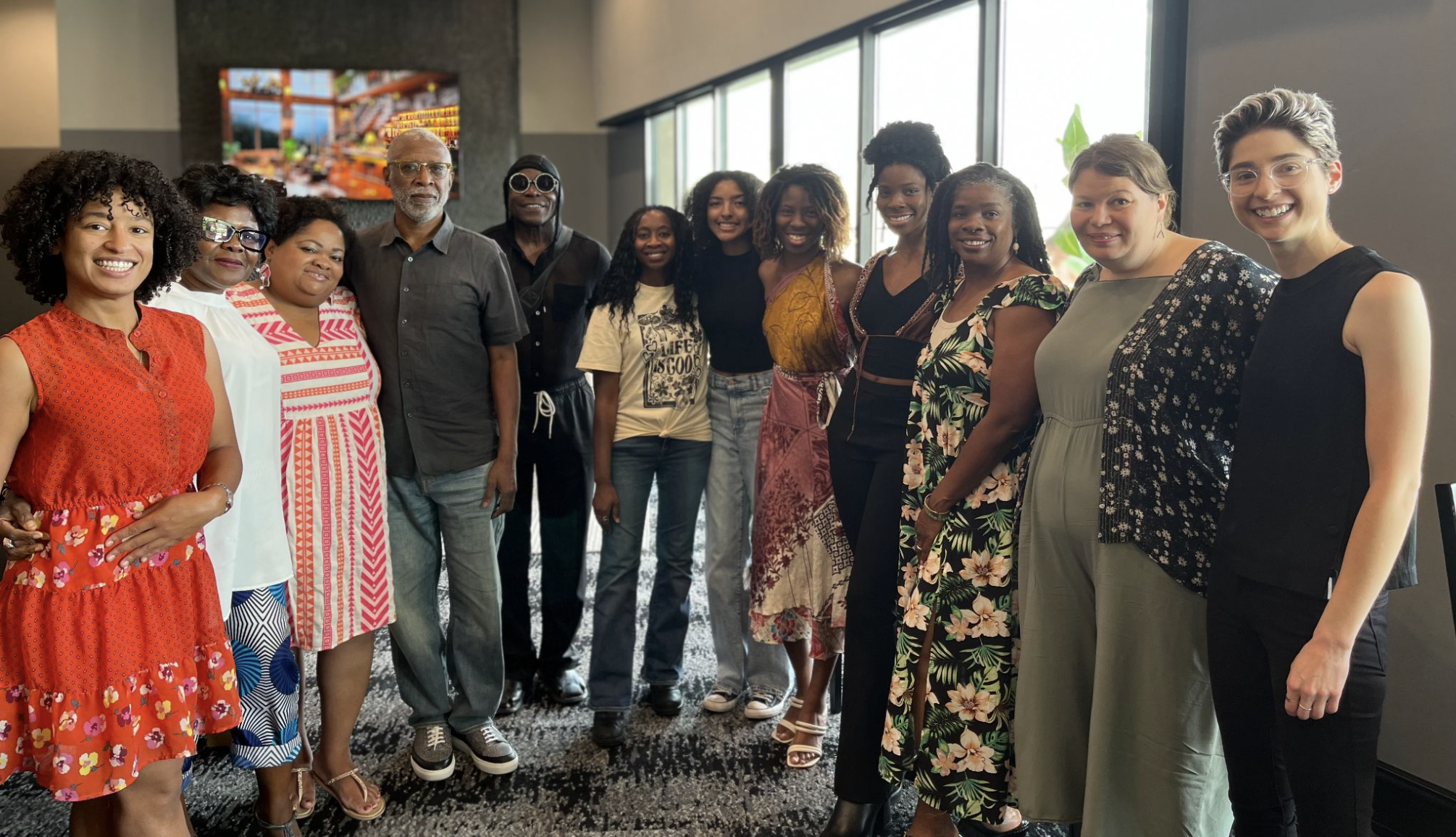 Group of diverse women and men posing together indoors, smiling, in casual and colorful clothing.