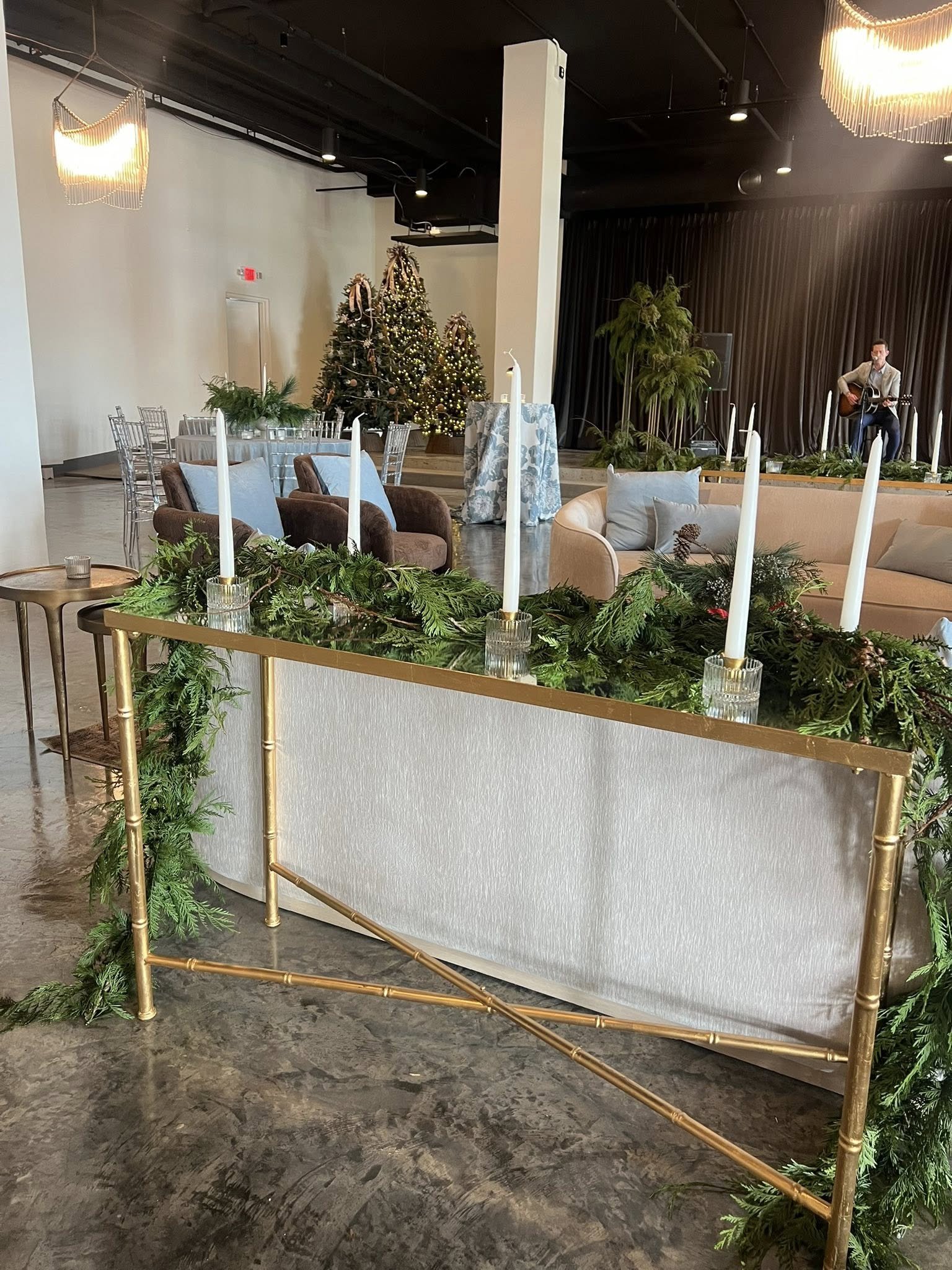 Seasonal event setup at The Velveteen wedding venue in Madison, MS, with decorated Christmas trees, candlelight, garlands, and a musician performing on the stage