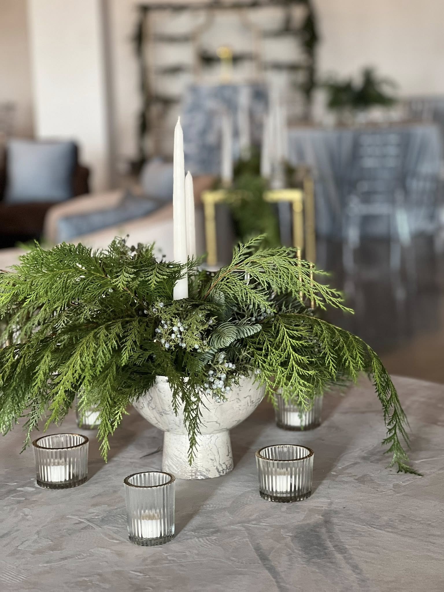 Holiday tablescape detail at The Velveteen in Madison, MS, featuring a white marble vase with greenery and white pillar candles, surrounded by smaller glass votives