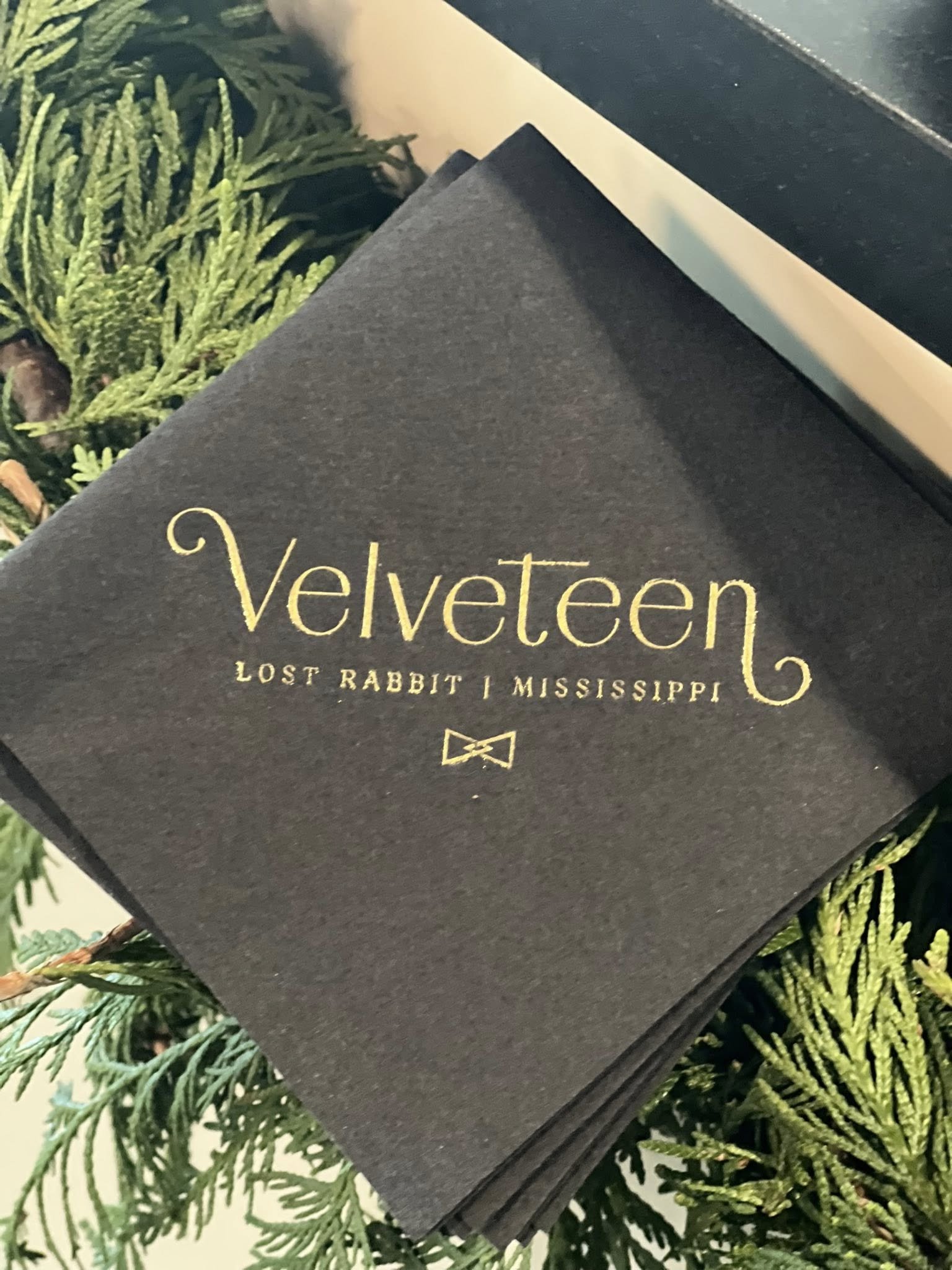 Custom Velveteen-branded gift box at The Velveteen wedding venue in Madison, MS, displayed among fresh evergreen garland with the Lost Rabbit, Mississippi label visible