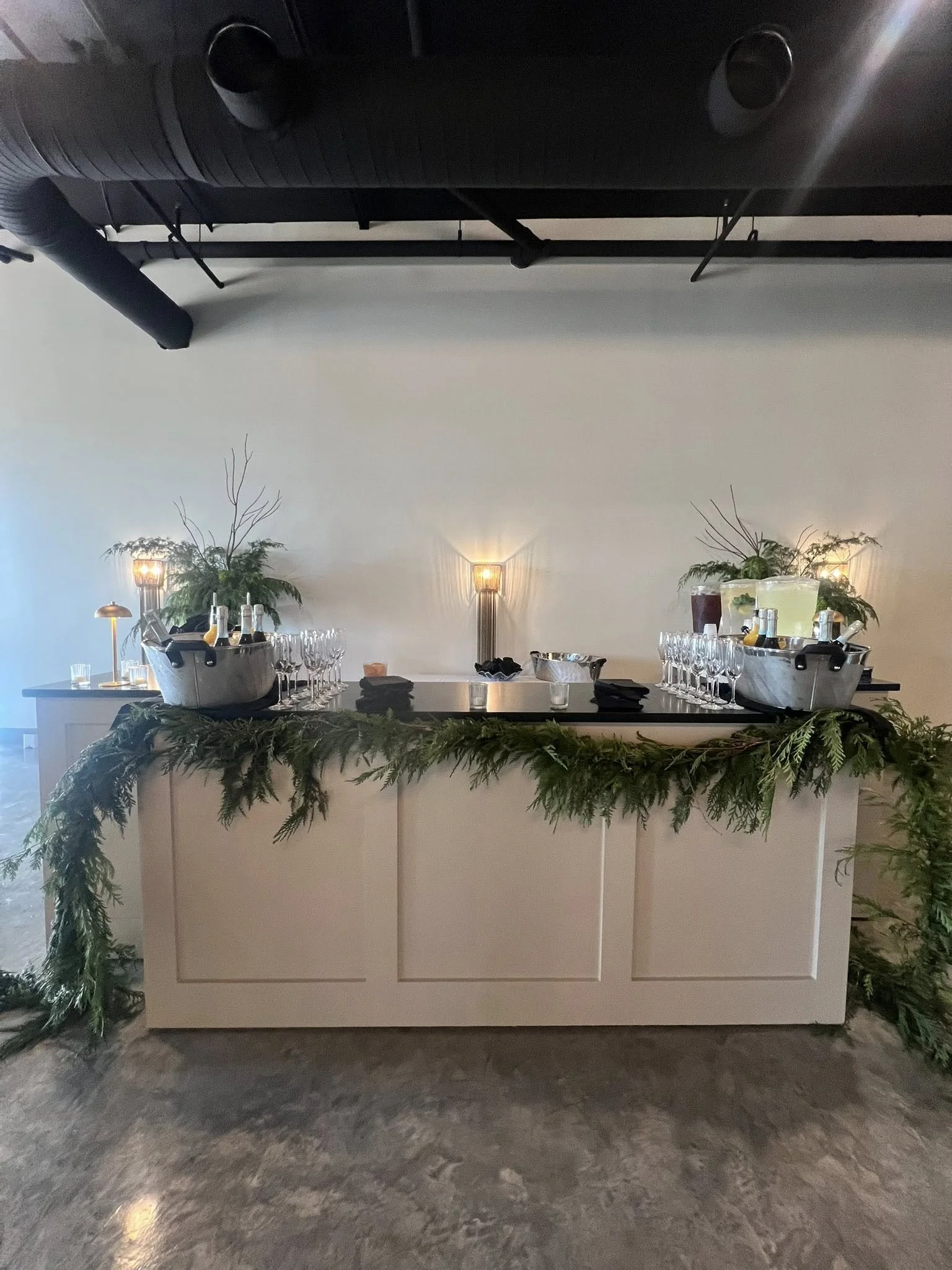 Bar service at The Velveteen wedding venue in Madison, MS, with chilled bottles in twin ice buckets, rows of wine glasses, and fresh greenery along the bar top