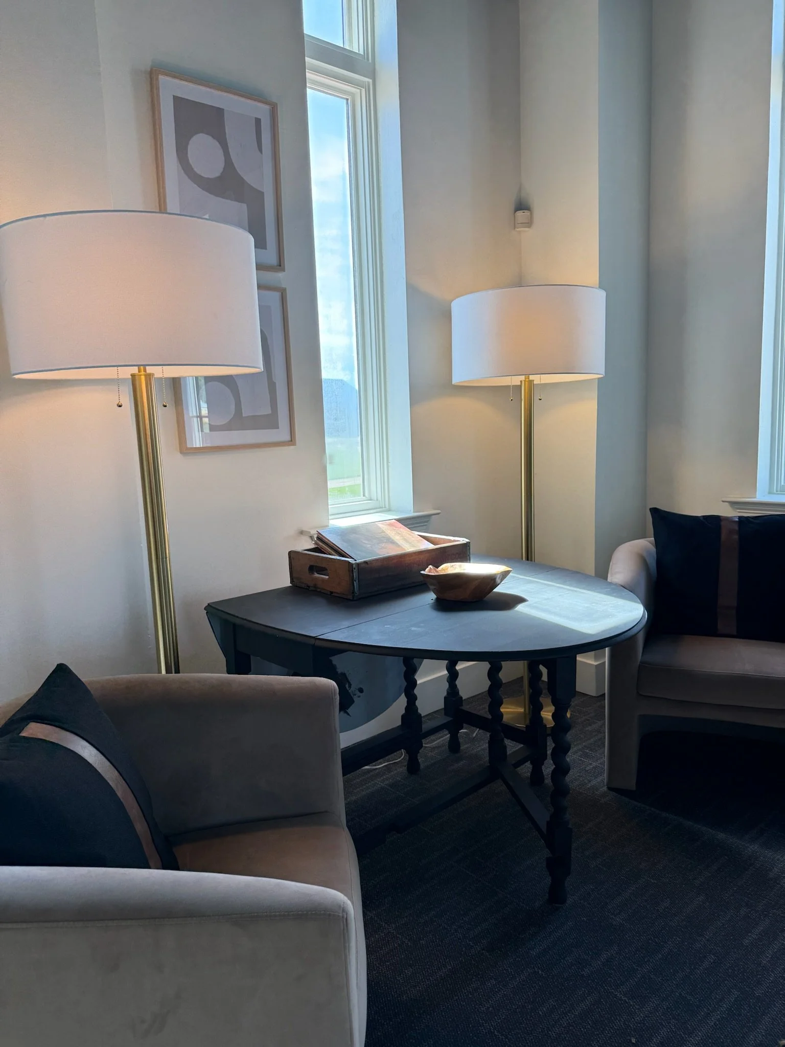 Bridal suite seating at The Velveteen wedding venue in Madison, MS, with a beige armchair, a dark wood pedestal table, and tall floor lamps framing a curtained window