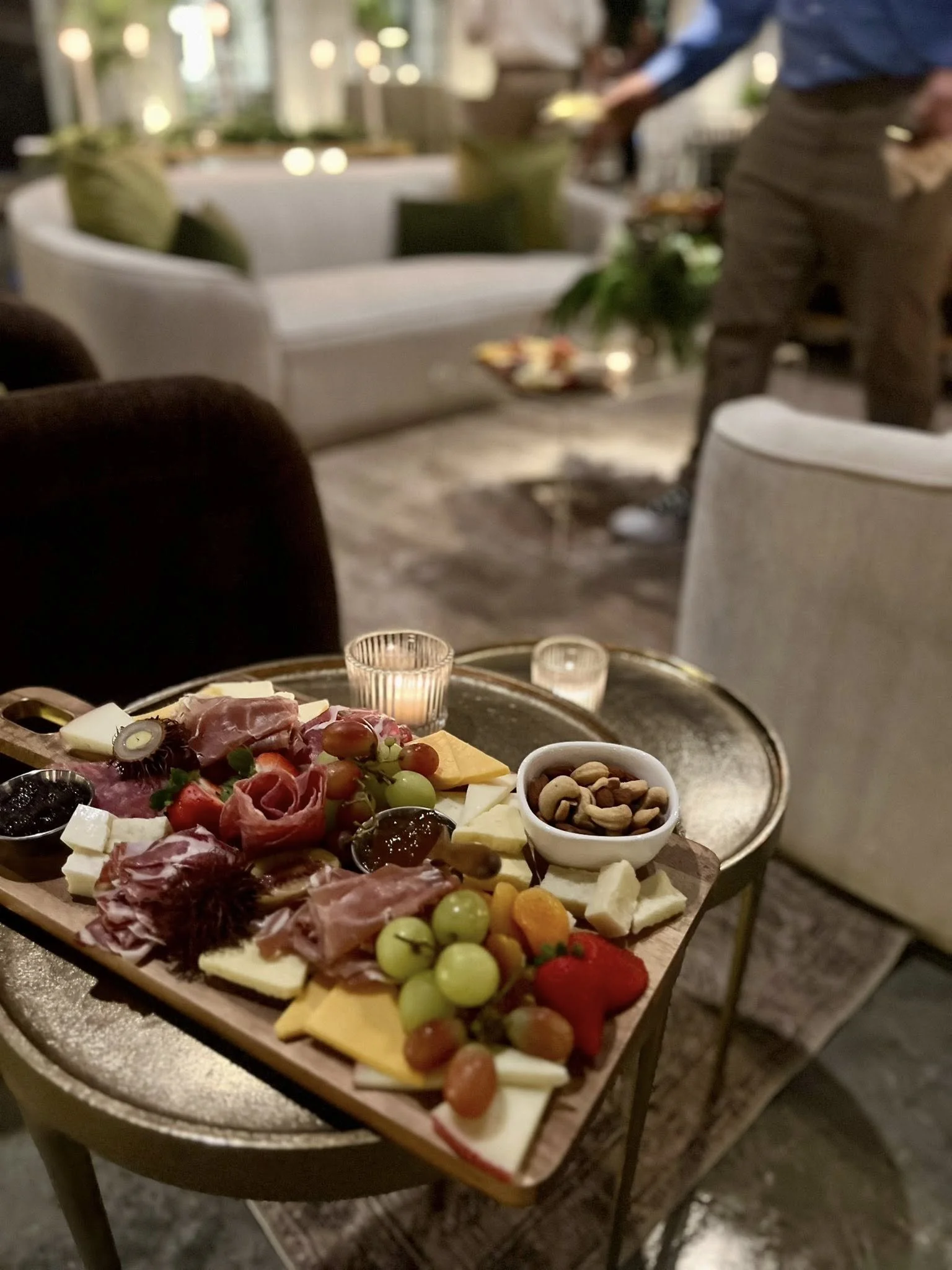 Charcuterie spread at The Velveteen in Madison, MS, with assorted cheeses, cured meats, fresh grapes, and nuts styled on a round table beside a glowing candle