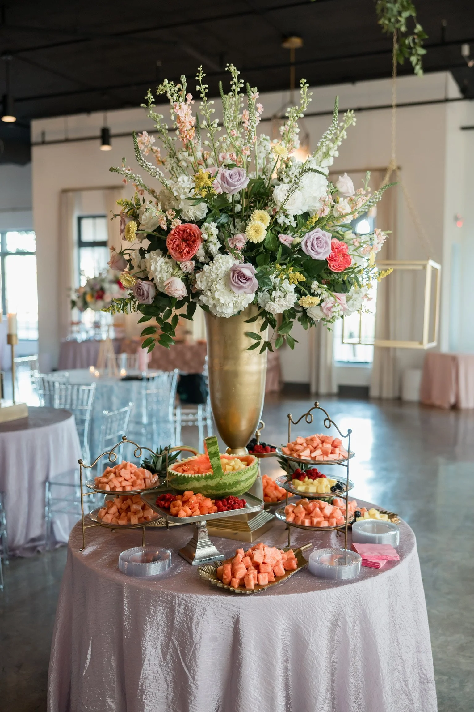 Tall floral arrangement with a tiered fruit display on a reception table at The Velveteen wedding venue in Madison, MS.