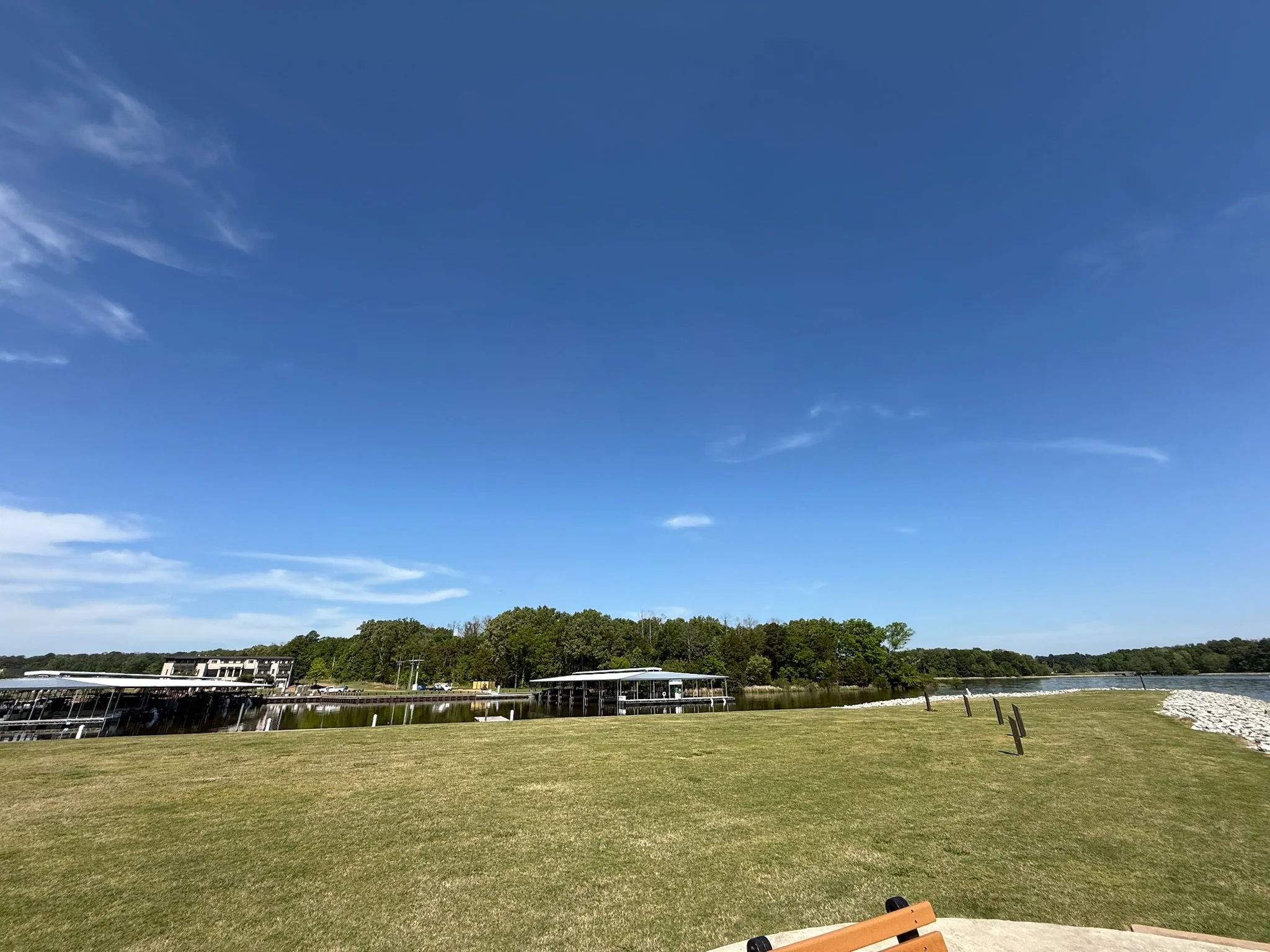 Waterfront grounds at The Velveteen wedding venue in Madison, MS, looking across an open lawn toward the lake and tree line under a clear blue sky