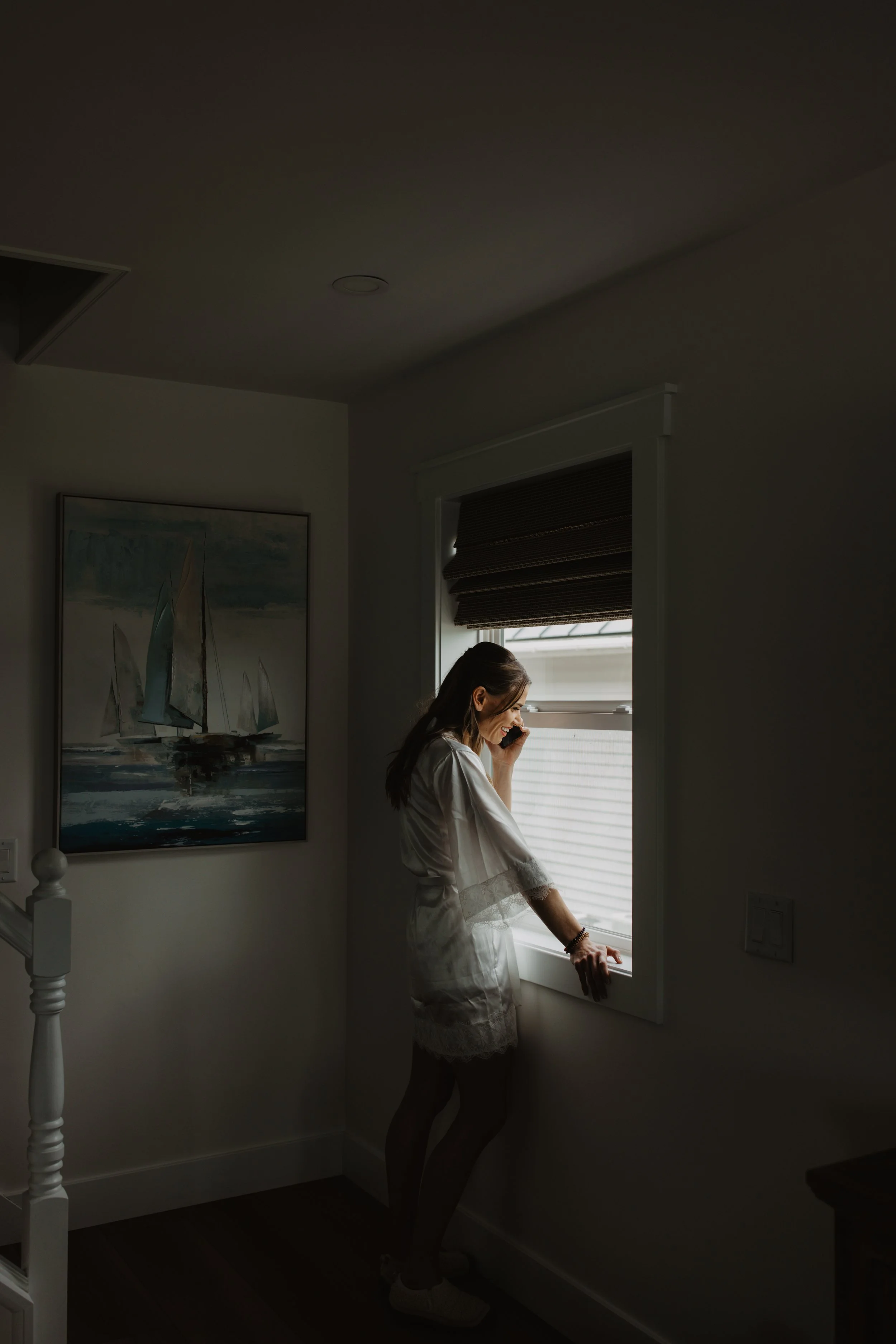 A woman standing by a window talking on a phone.