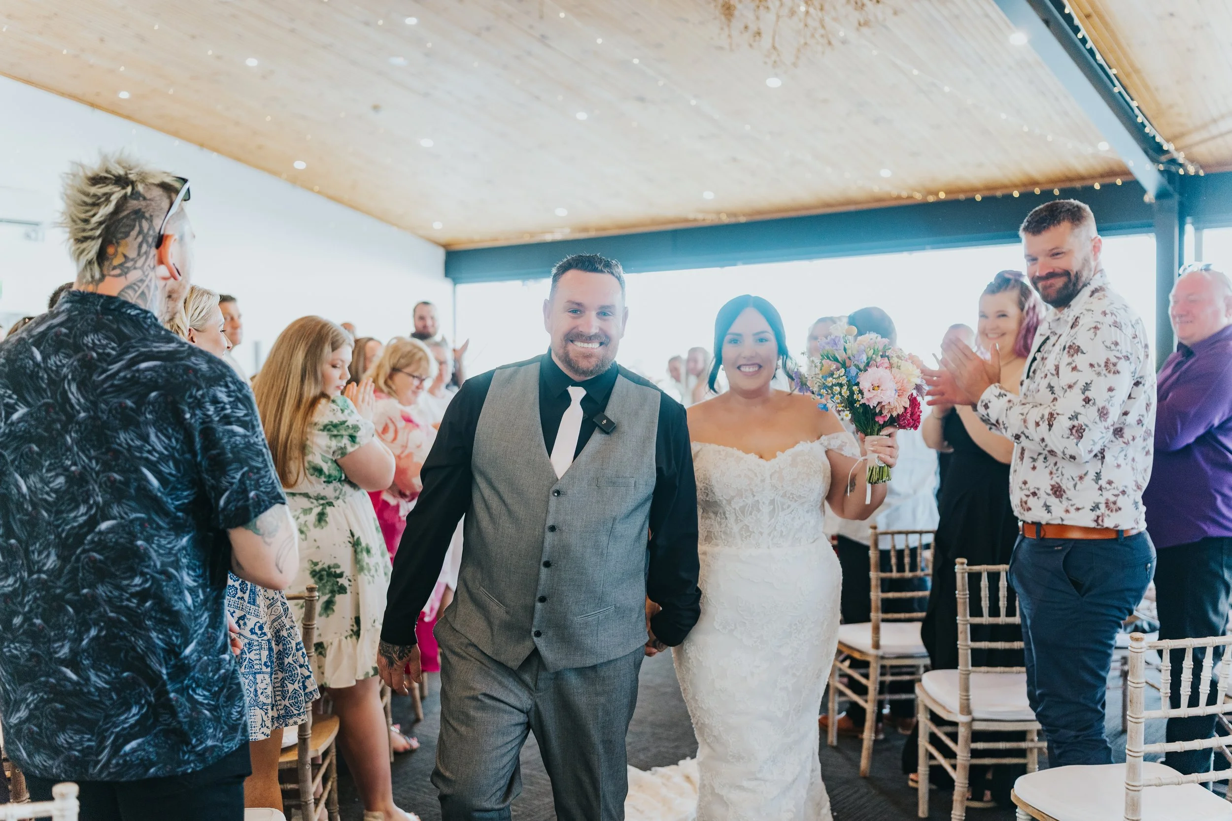 Bride and groom walking down the aisle at their wedding, surrounded by friends and family clapping and smiling.
