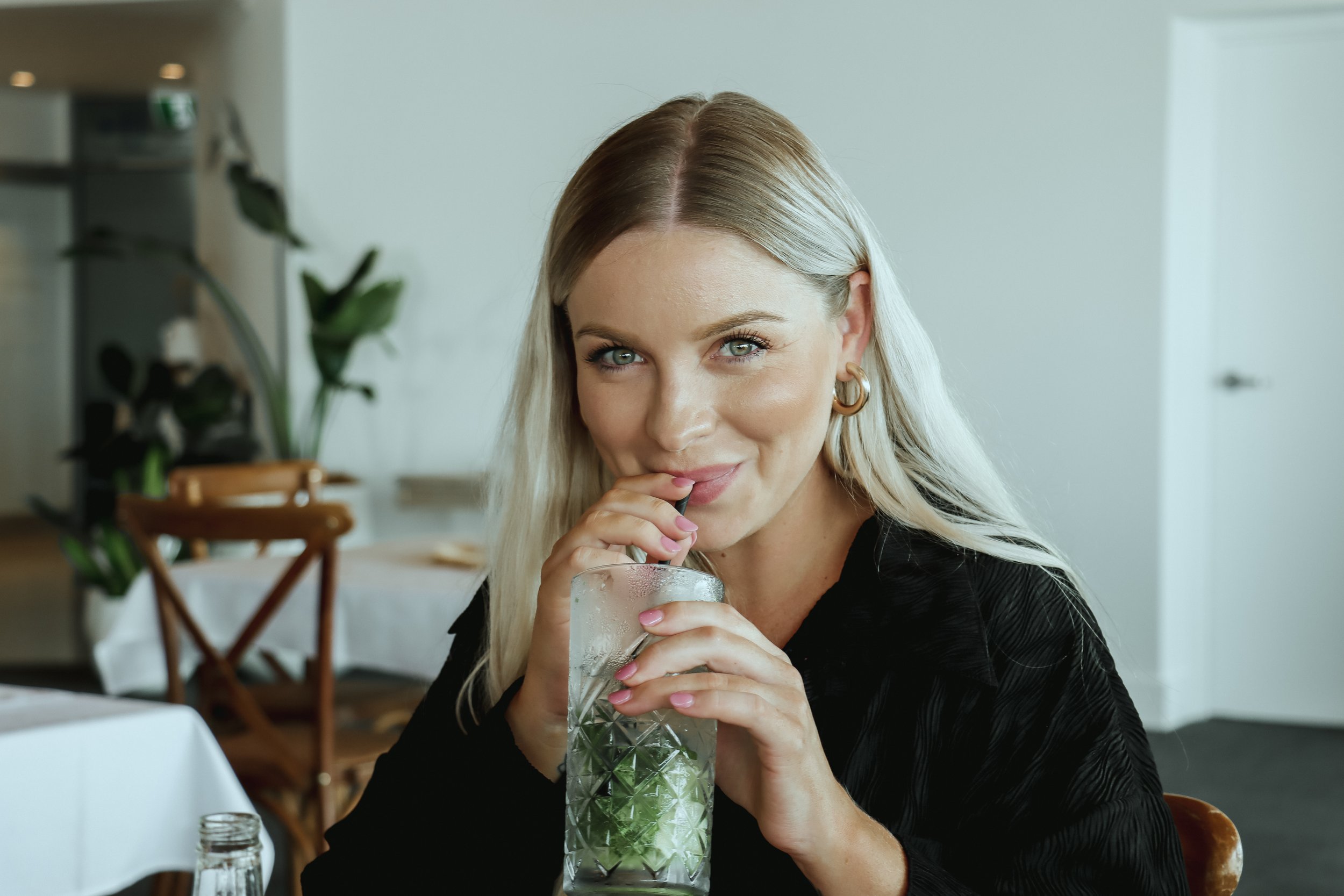 A woman drinking a beverage through a straw in a restaurant or café setting.